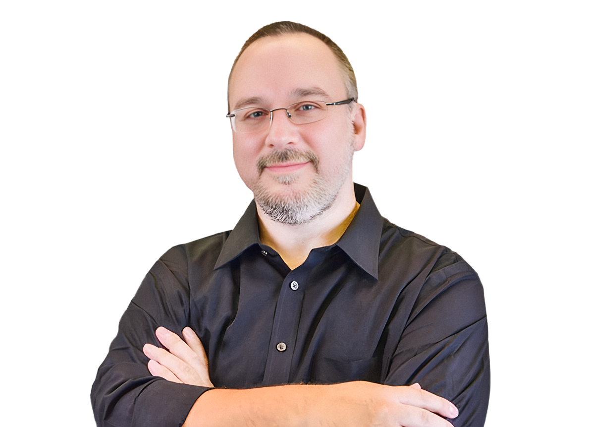A middle-aged man with glasses, a beard, and a mustache, wearing a black shirt, standing with arms crossed and smiling.