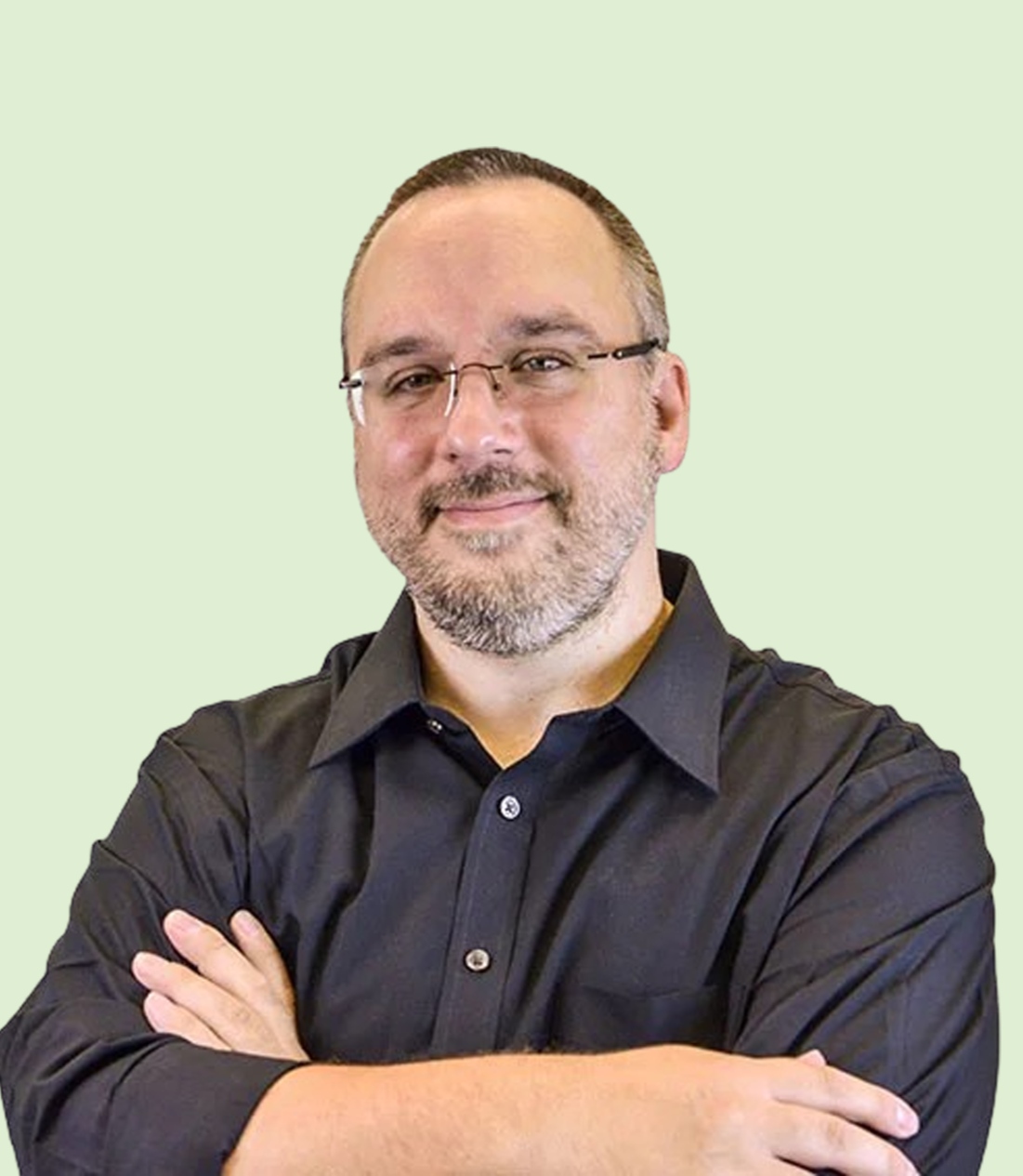 A man with glasses, a beard, and a mustache, wearing a black shirt and smiling with arms crossed on a light green background.