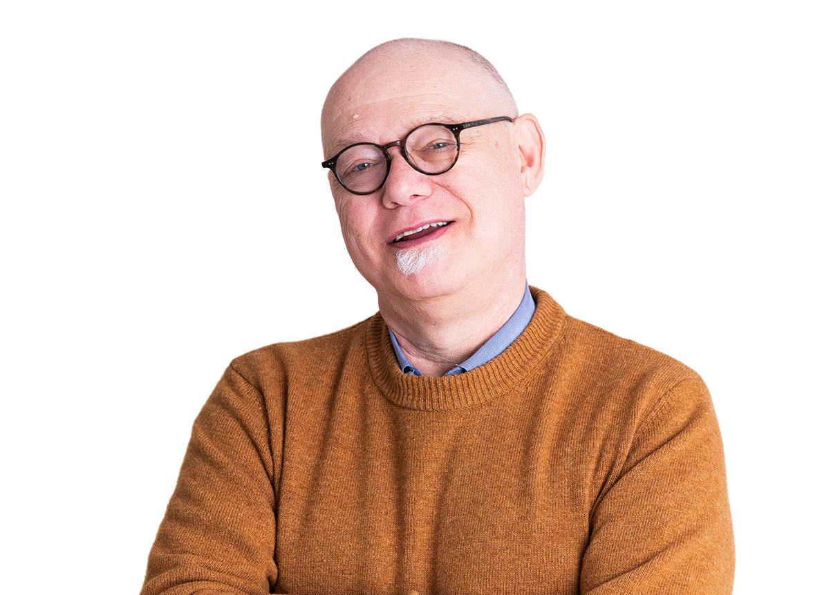 A middle-aged man with a bald head, glasses, and a white goatee, wearing a mustard-colored sweater and a blue collared shirt, smiling with his arms crossed.