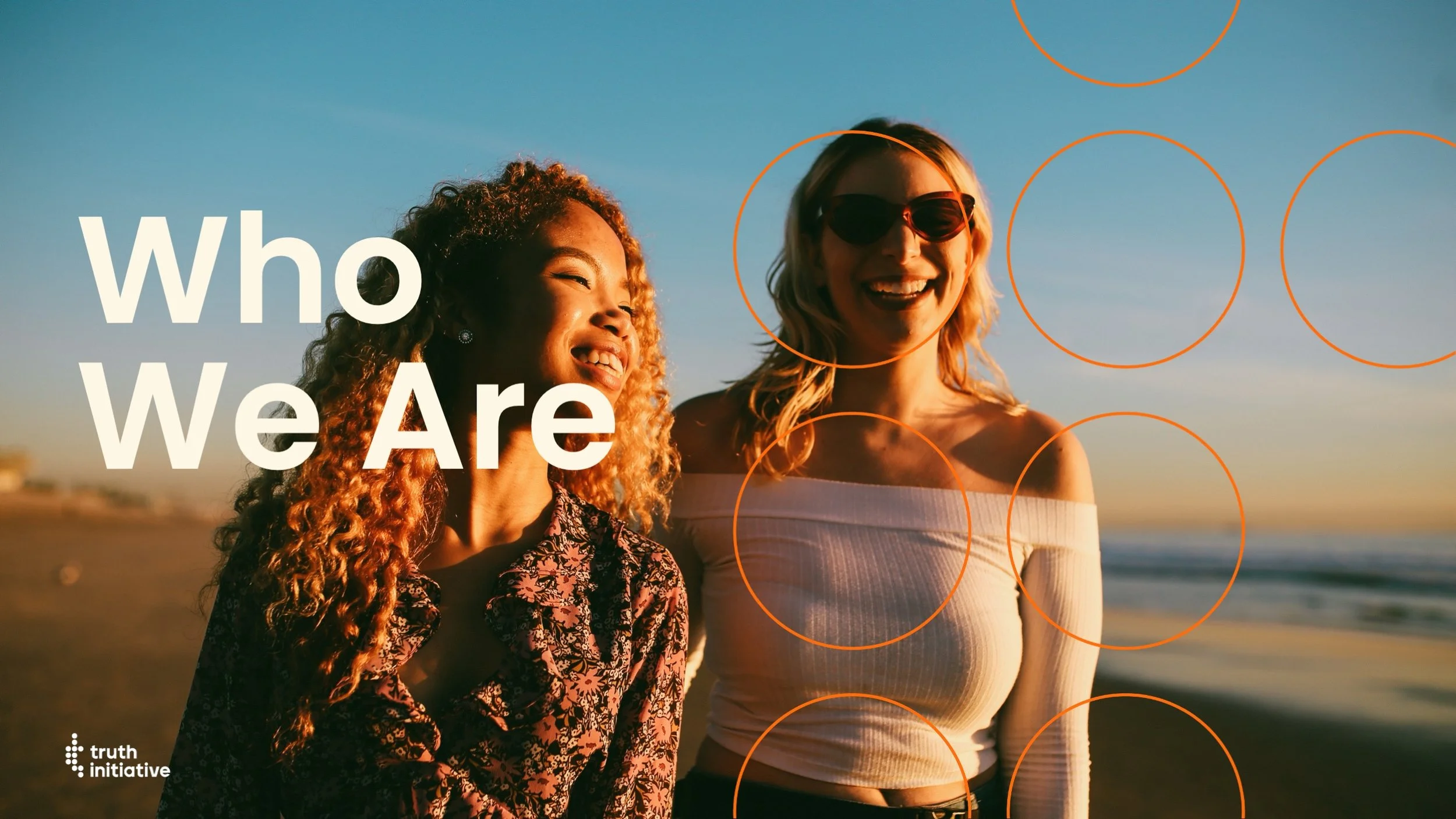 Two women smiling and standing on a beach during sunset, with the text 'Who We Are' overlaid and orange circles in the background.