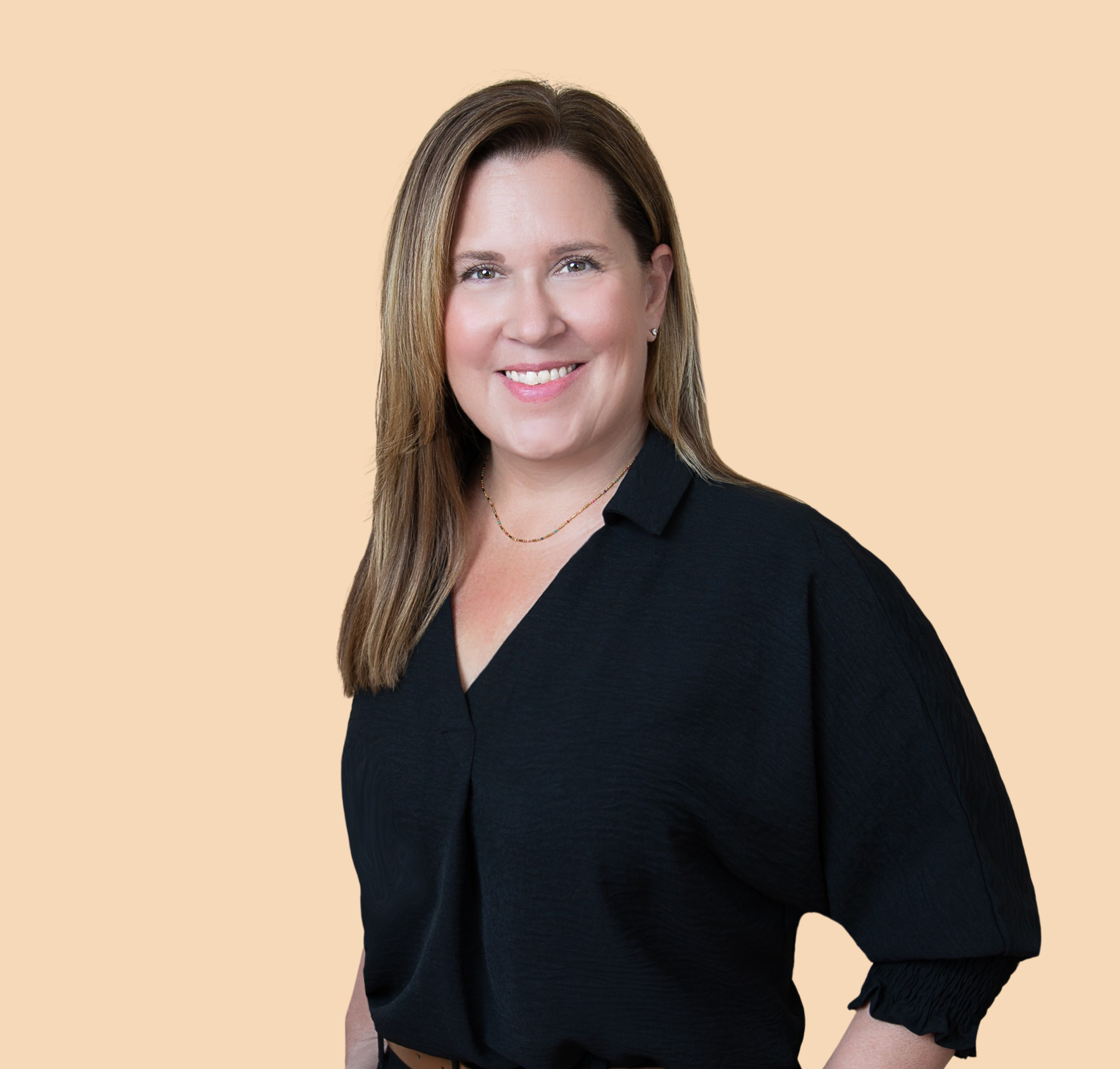 A woman with long brown hair, wearing a black top, smiling for a portrait against a beige background.