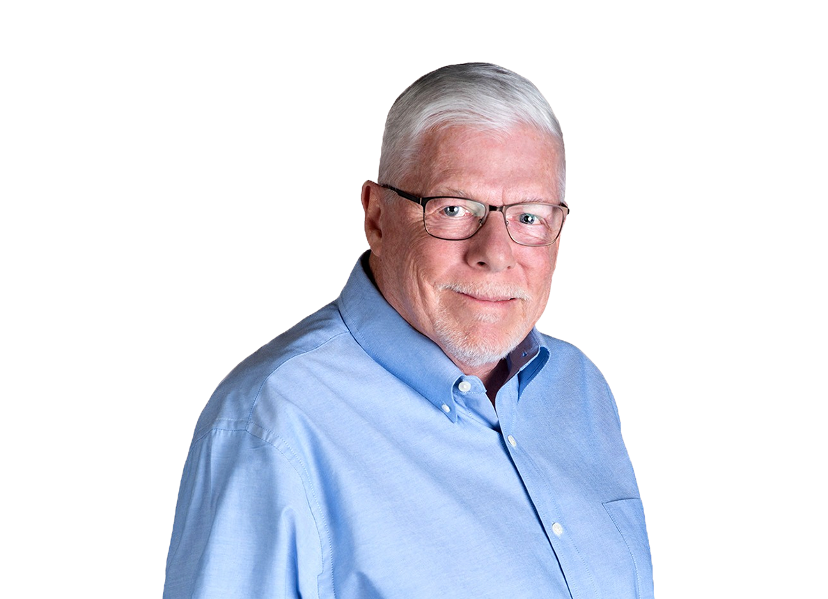 Older man with glasses and white hair smiling, wearing a blue collared shirt against a black and gray background.