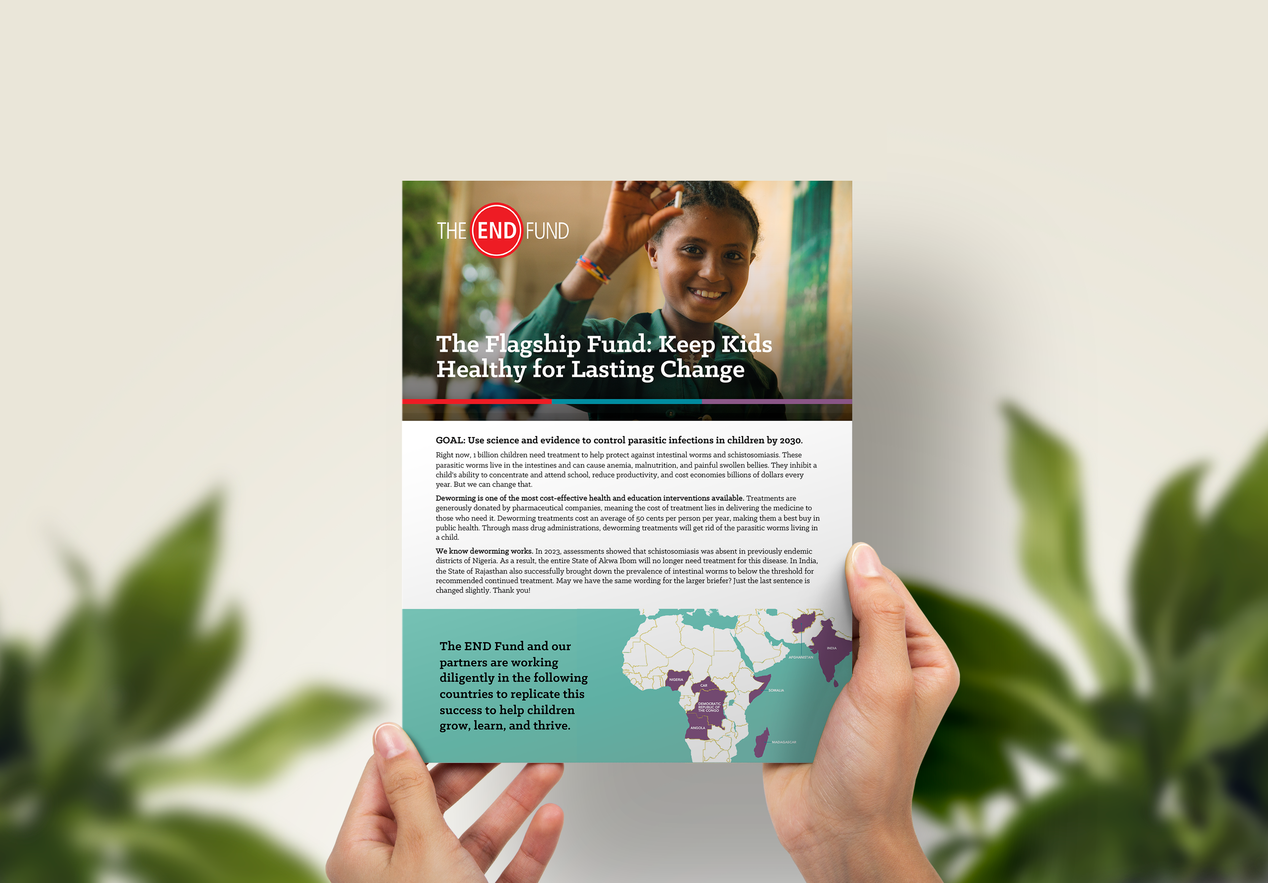 A person holding a printed webpage about the END Fund, which focuses on children's health and parasite control, with a woman smiling in the background.