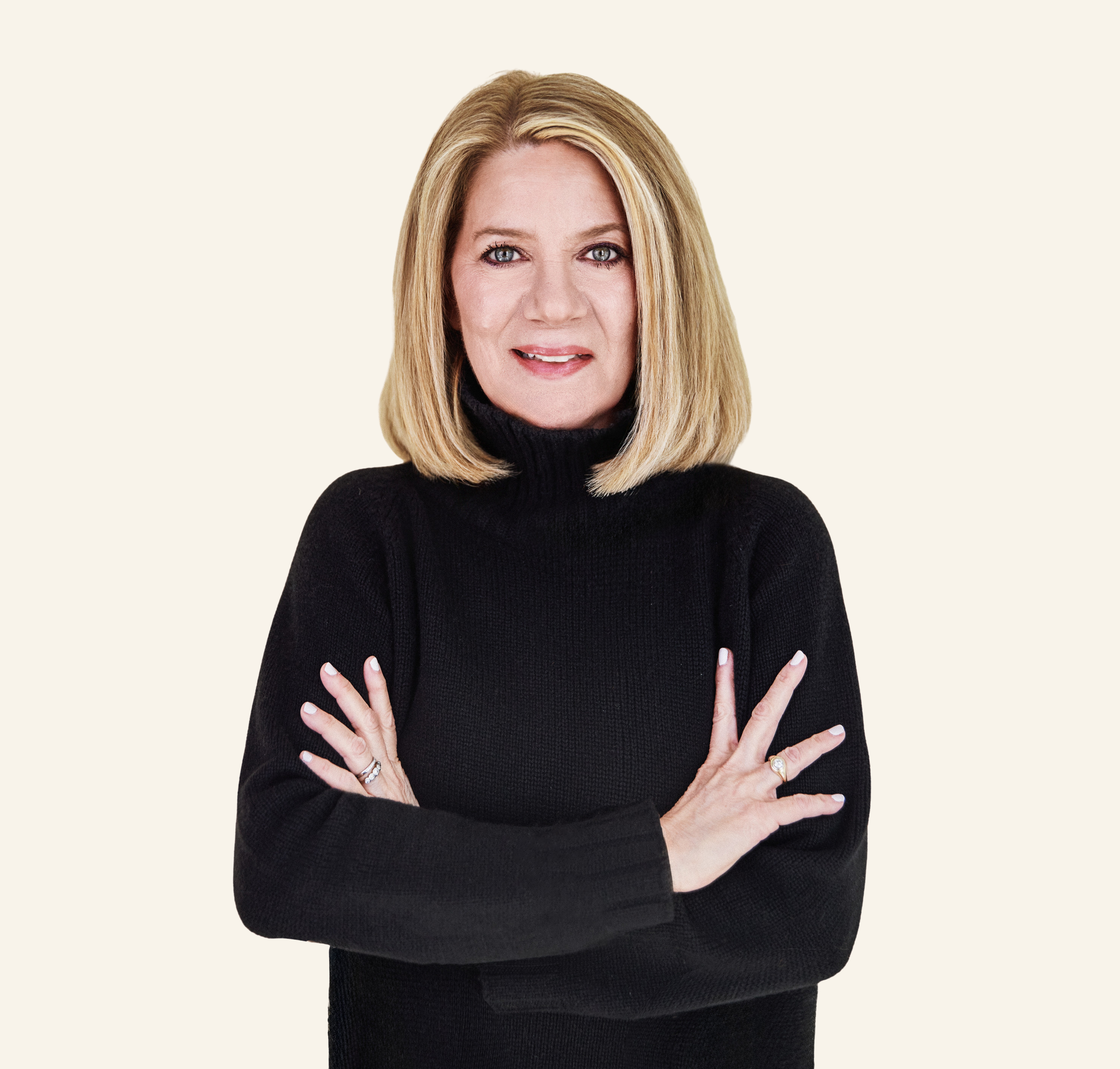 Portrait of a woman with shoulder-length blonde hair wearing a black turtleneck sweater, standing against a plain light background.