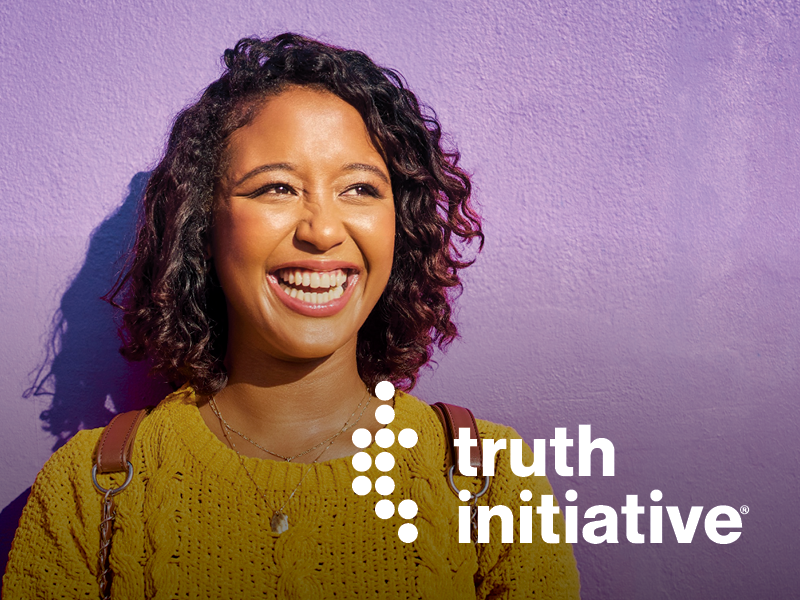 A woman smiling and looking to the side against a purple wall, with the words "truth initiative" and a dotted design in the lower right corner.
