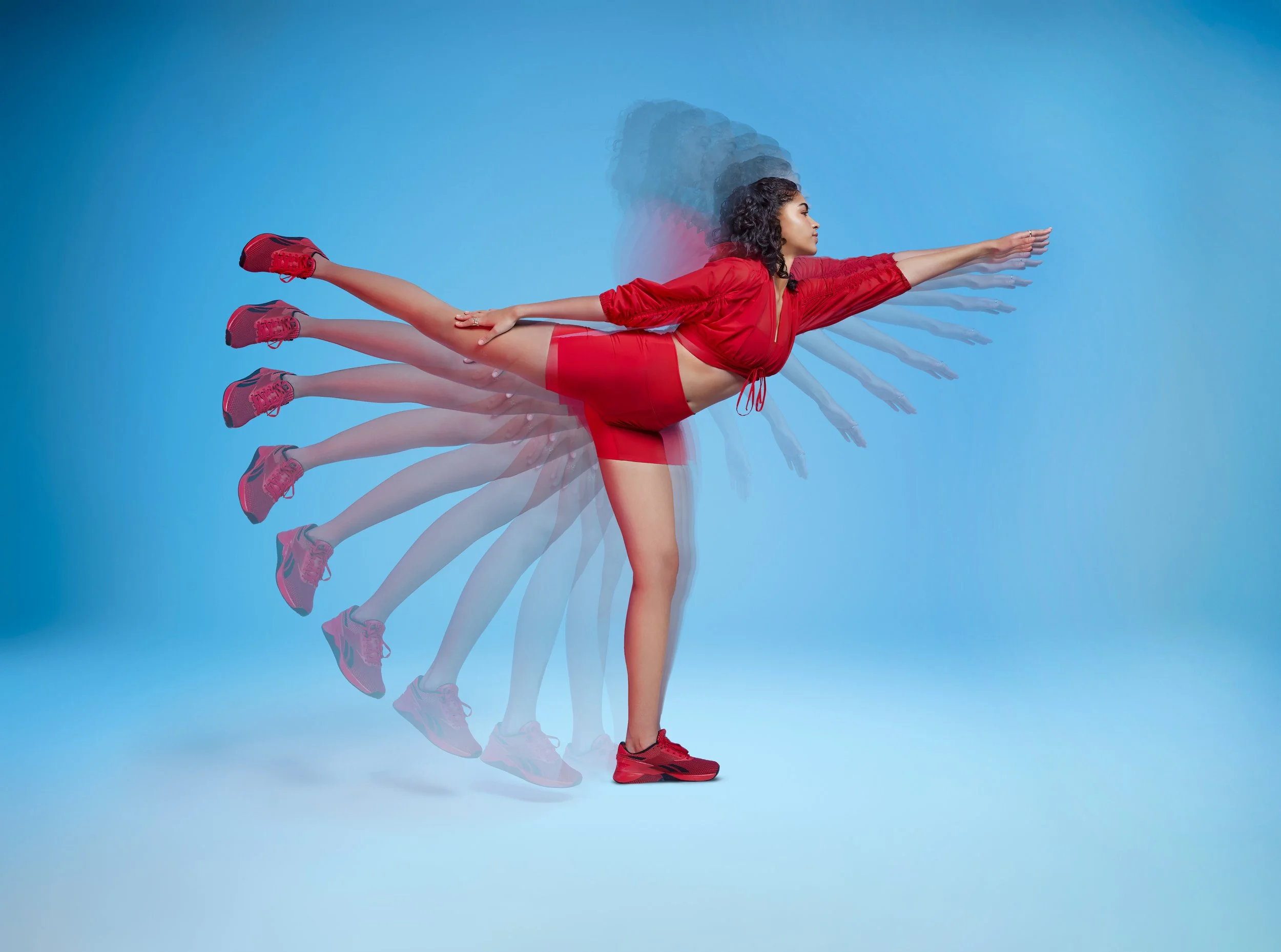 A woman in a red athletic outfit and sneakers performs a forward bend yoga pose, with motion blur creating multiple overlapping images against a blue background.