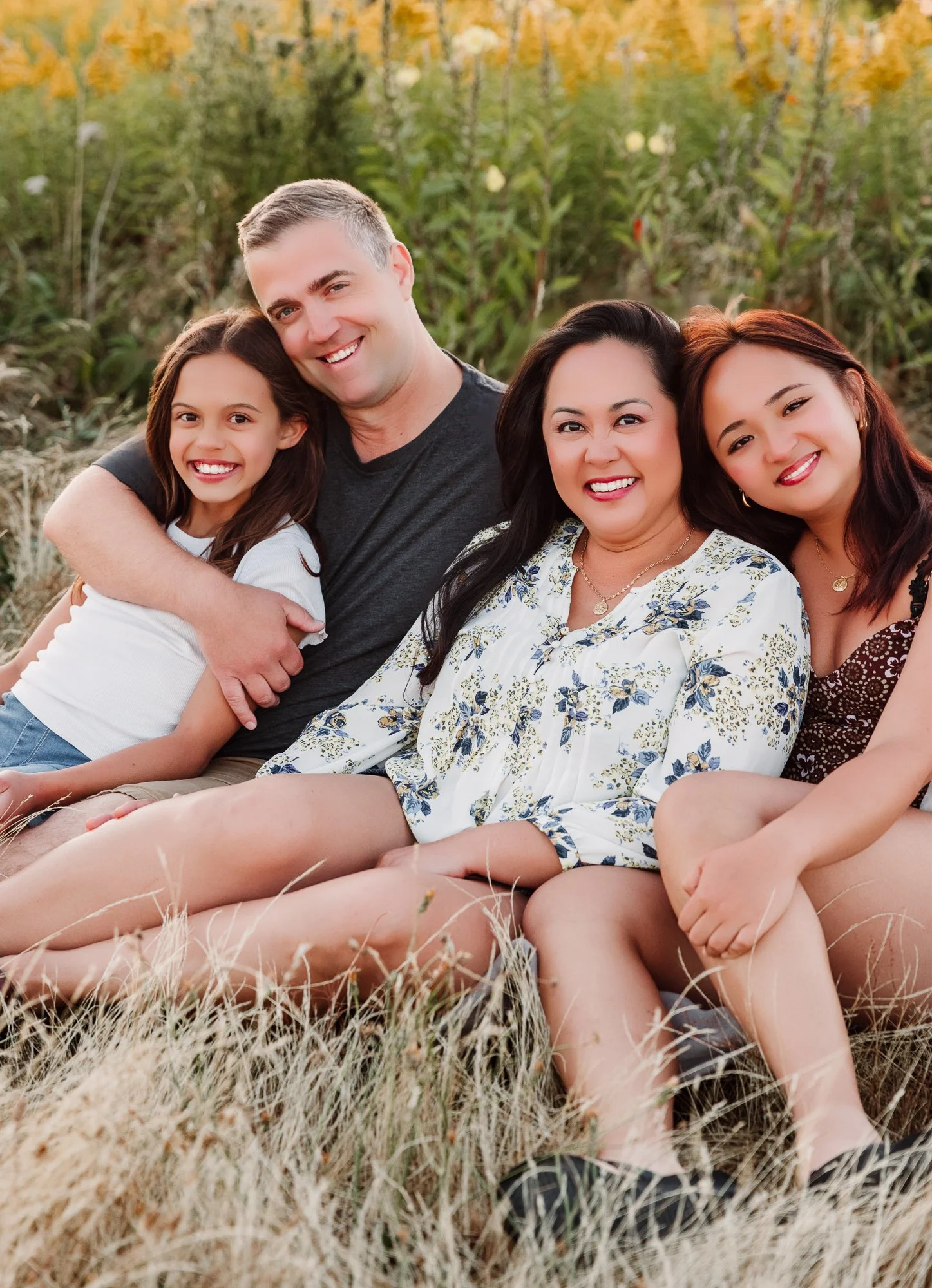 Family sitting together in long grass at sunset, smiling, at Garry Point Park, Richmond, BC.