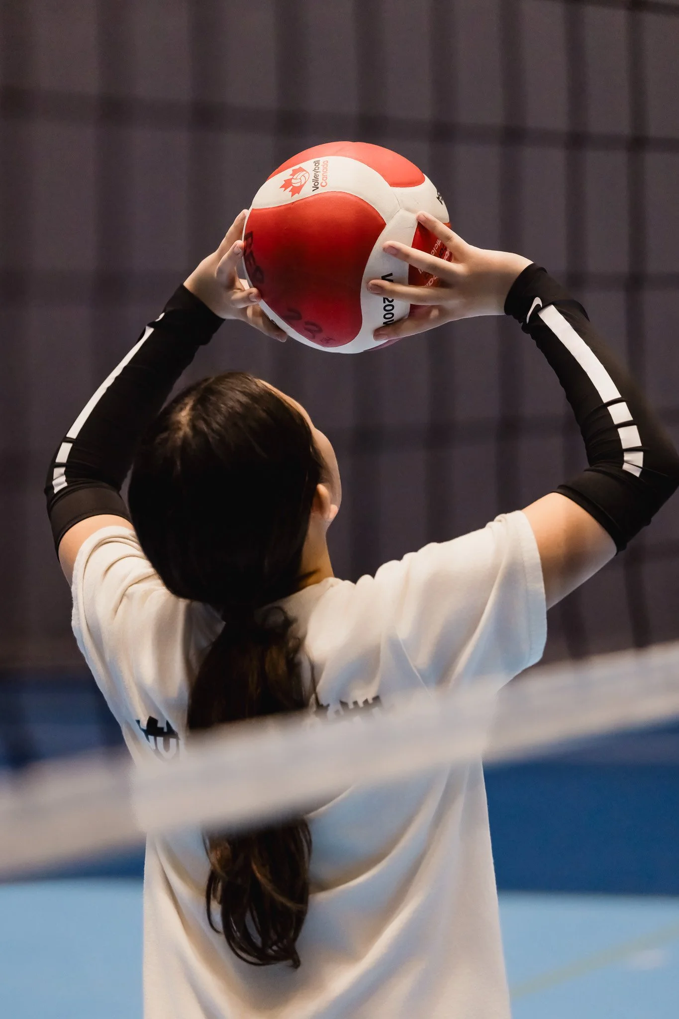 A volleyball player holding a red and white volleyball during a game at Richmond Olympic Oval.