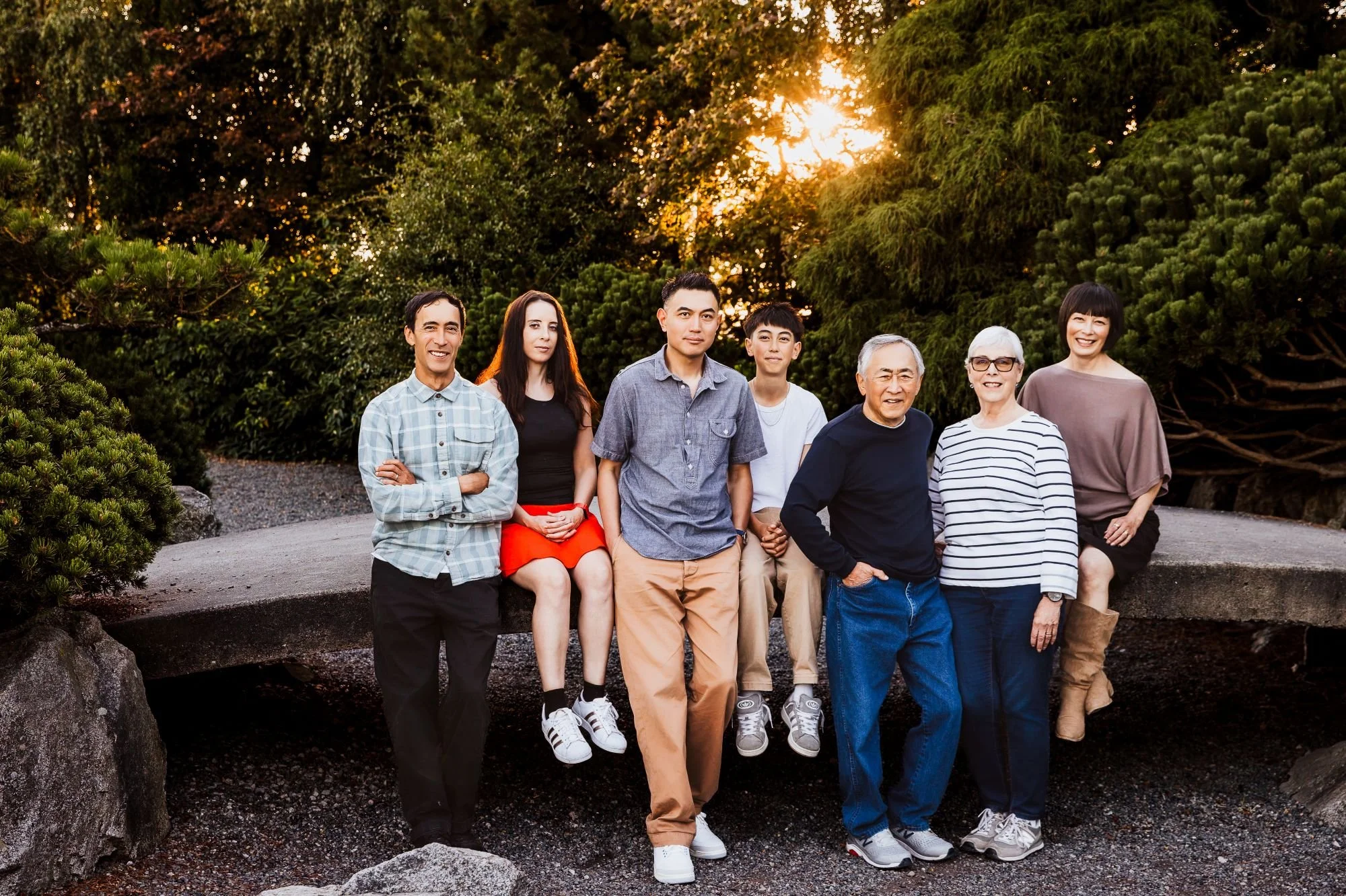 Group of eight diverse people standing outdoors in a lush green park during sunset, smiling and posing for the photo at Garry Point Park, Richmond, BC by family photographer Michelle Baril Photography.