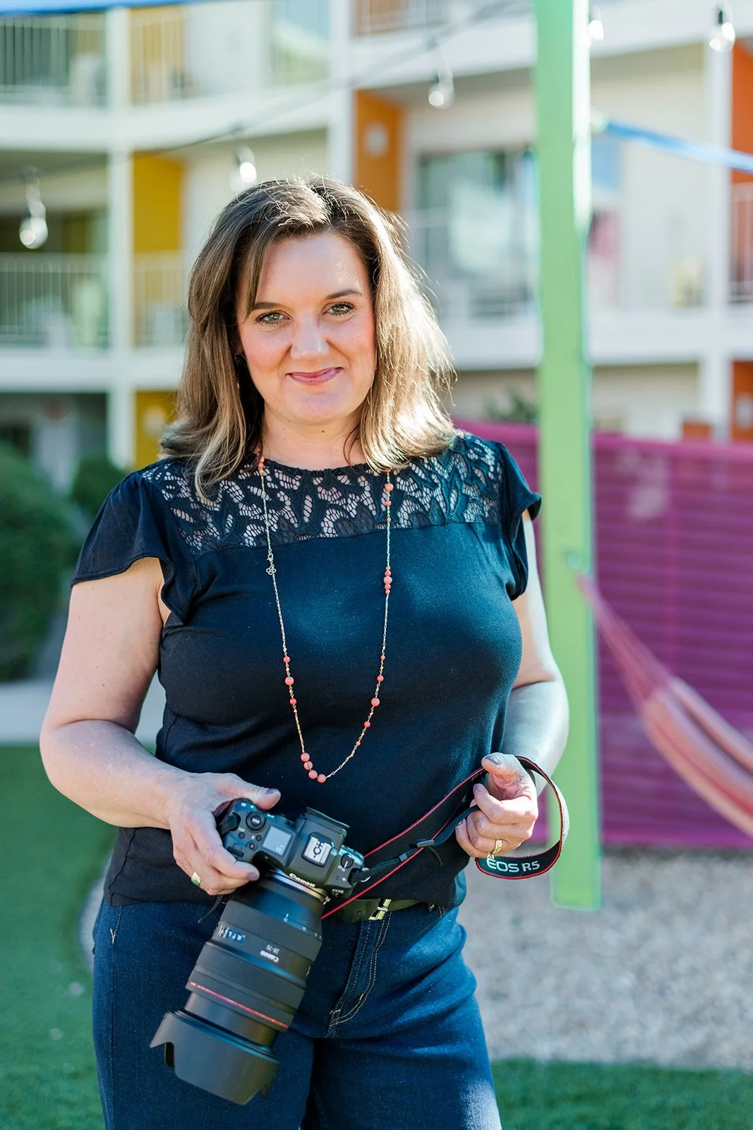 A woman standing outdoors holding a professional camera with a large lens. Portrait of Michelle Baril Photography.