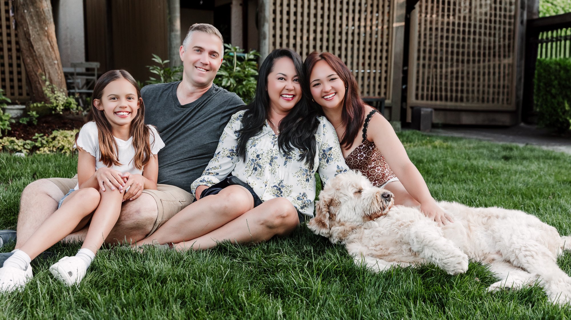 Family with dog sitting on the grass looking at the camera with Richmond Family Photographer Michelle Baril.