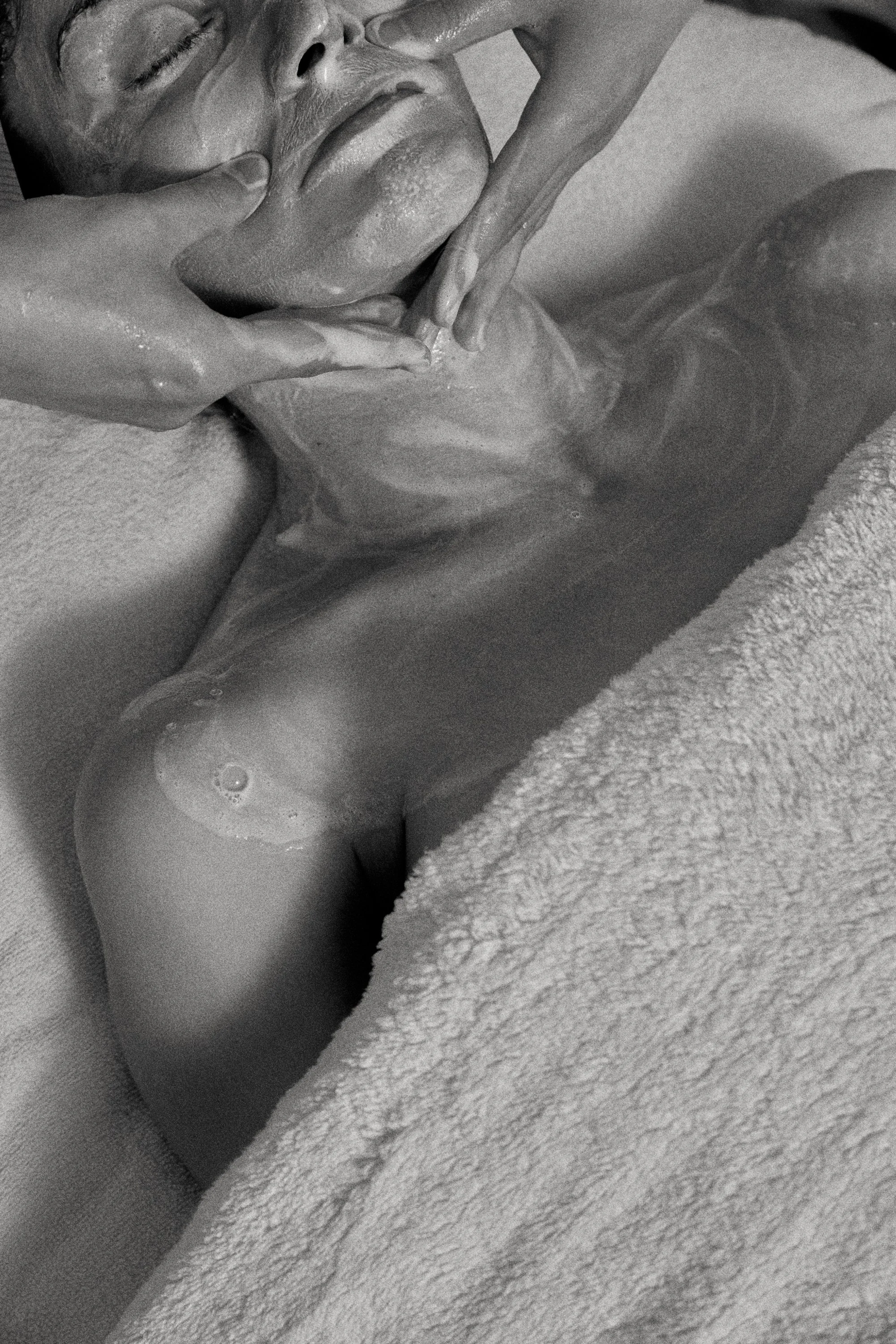 Person receiving a facial massage, covered with a towel, eyes closed.