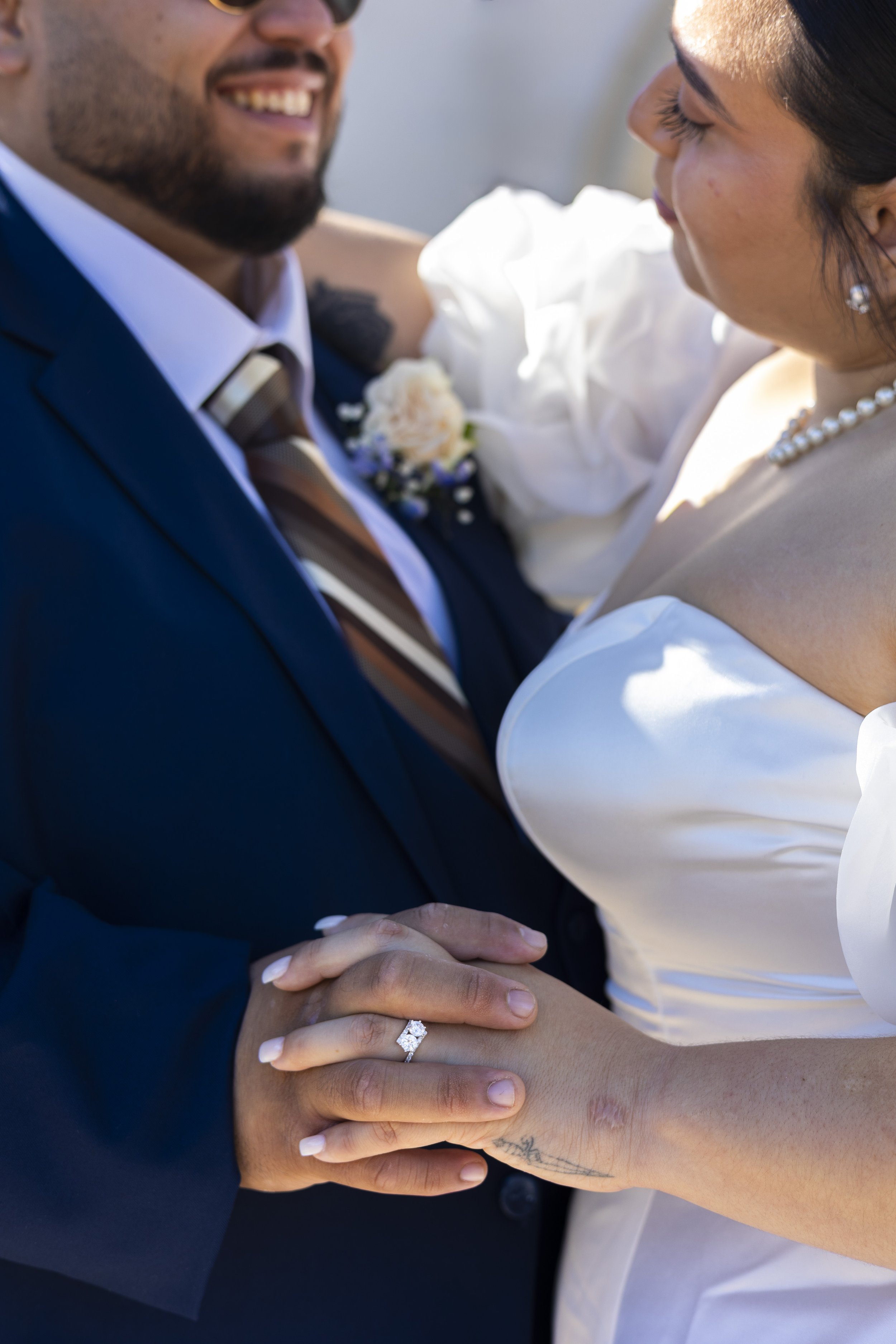 A close-up of a newlywed couple holding hands, showcasing a diamond engagement ring and wedding band, during their wedding celebration.