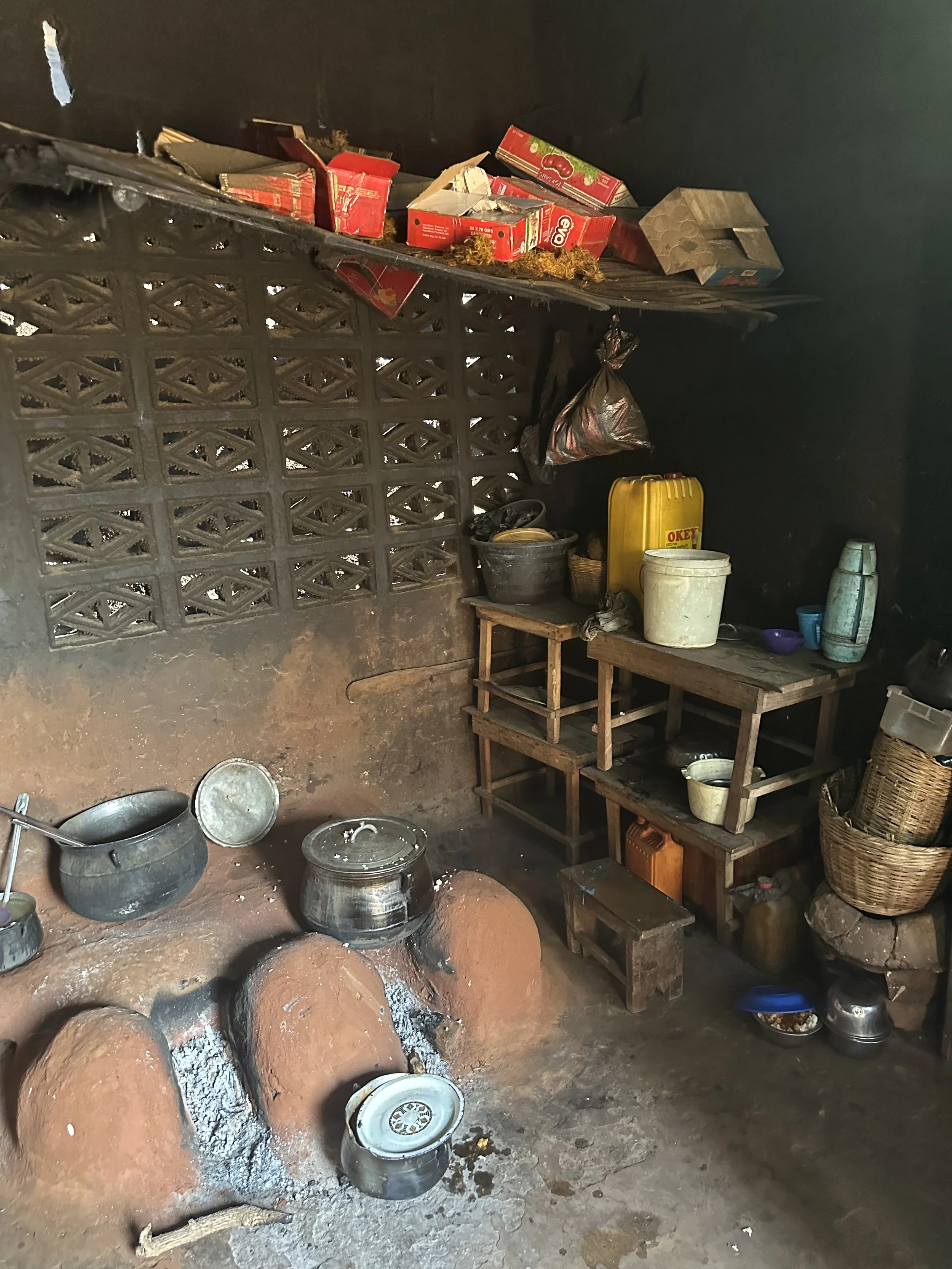 Simple kitchen with clay stove, pots, and shelves for kitchen items in a modest home.