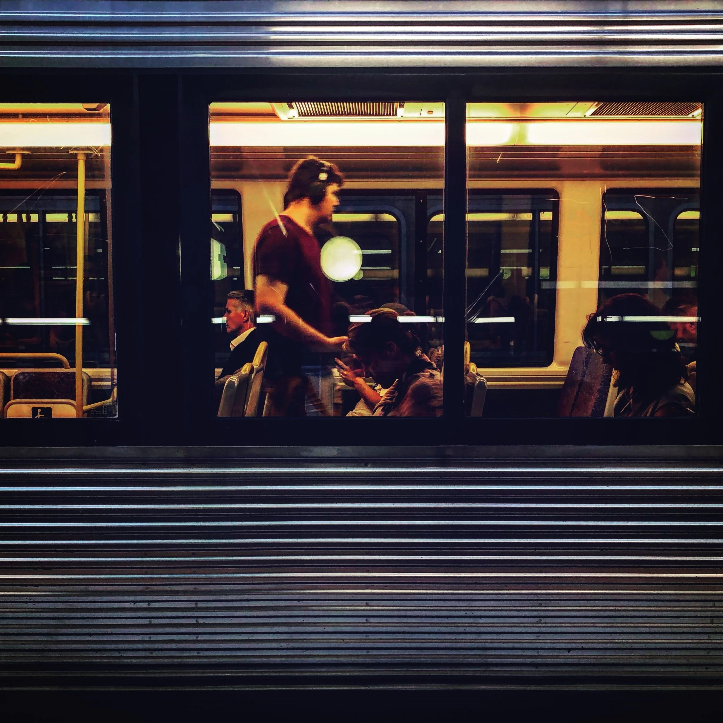 This is a photo taken by Jennine Heymer on a train. People sitting inside a train, viewed through the window, with a worker standing and talking to a passenger