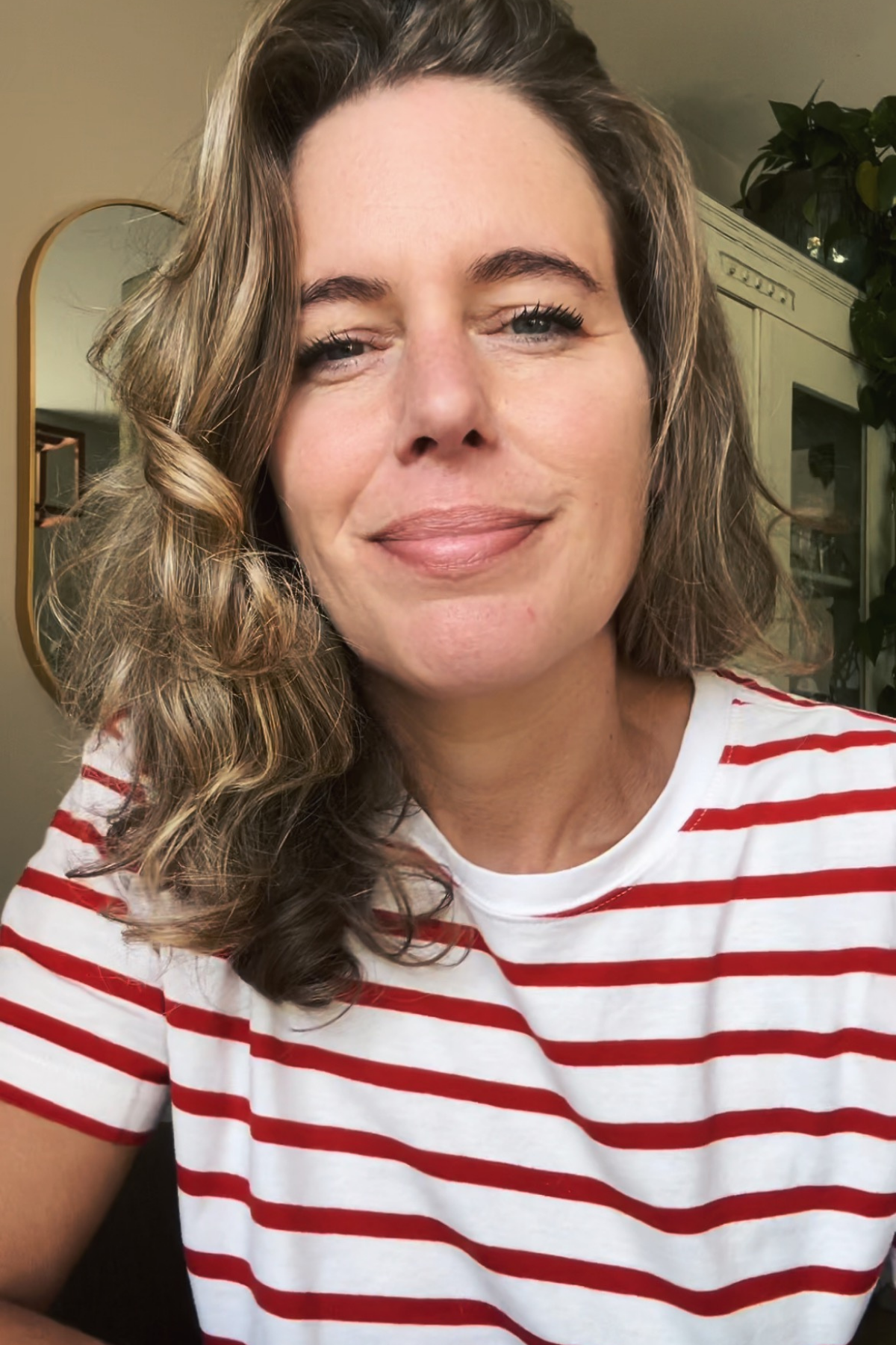 Close-up van een vrouw met golvende_BR hair in een zomeroutfit, lachend, in een binnenomgeving met planten