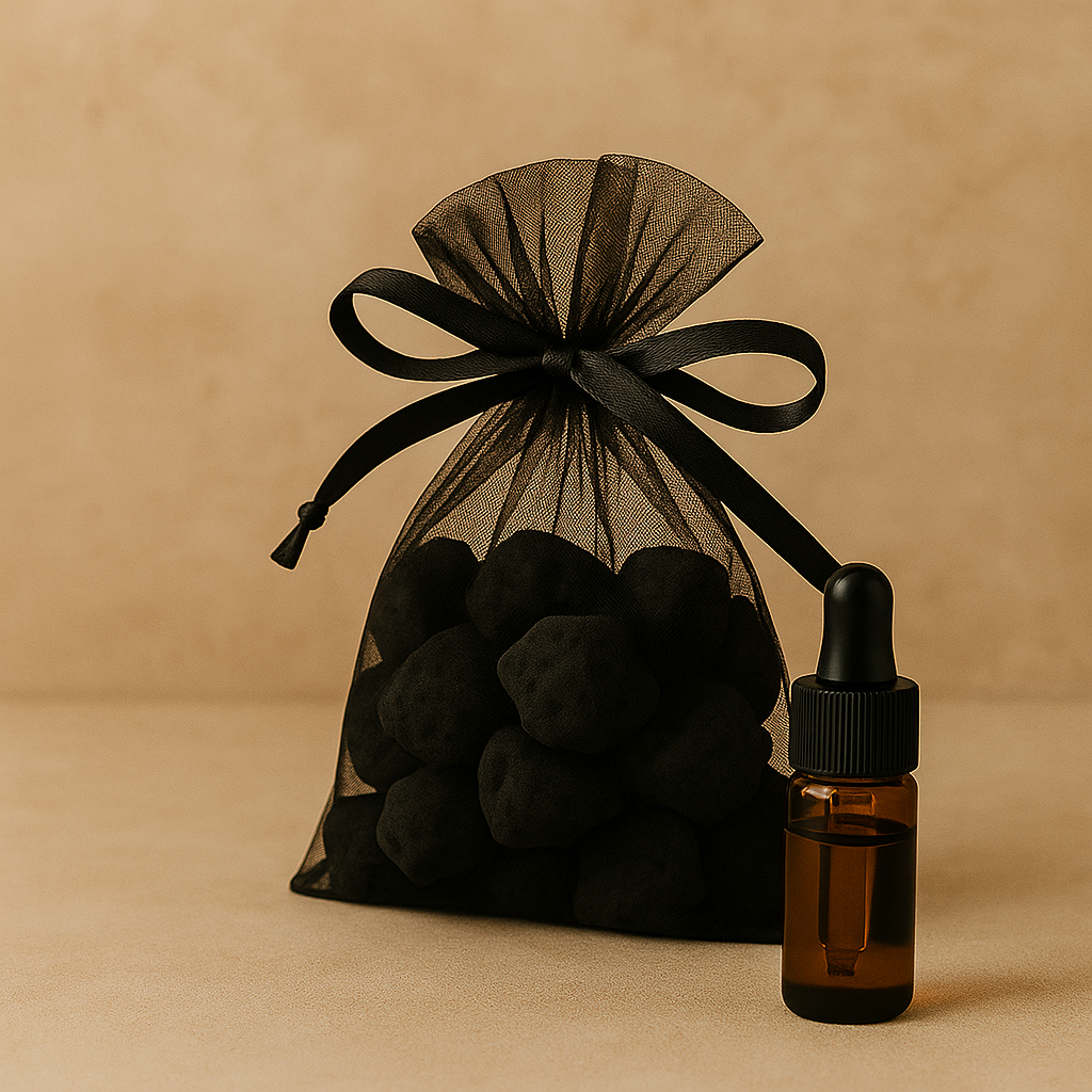 A black organza gift bag filled with black truffles and a small amber glass dropper bottle with a black cap, set on a beige surface against a beige background.