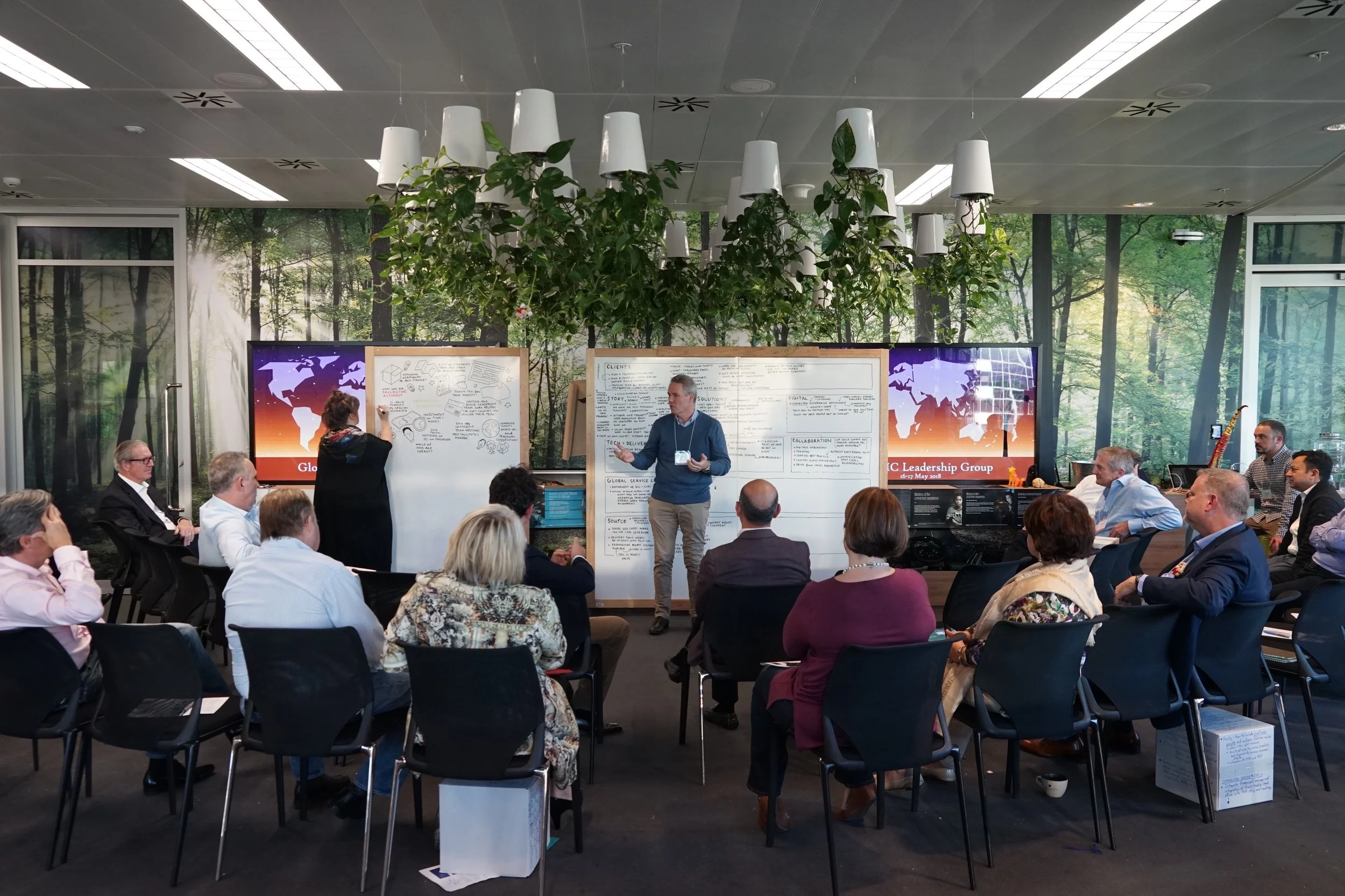 Presenter speaking in innovation lab with Kate Baxter creating a graphic recording  on whiteboard