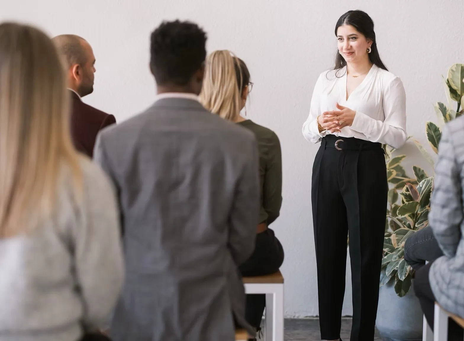 A woman in a white blouse stands in front of a group, giving a presentation.
