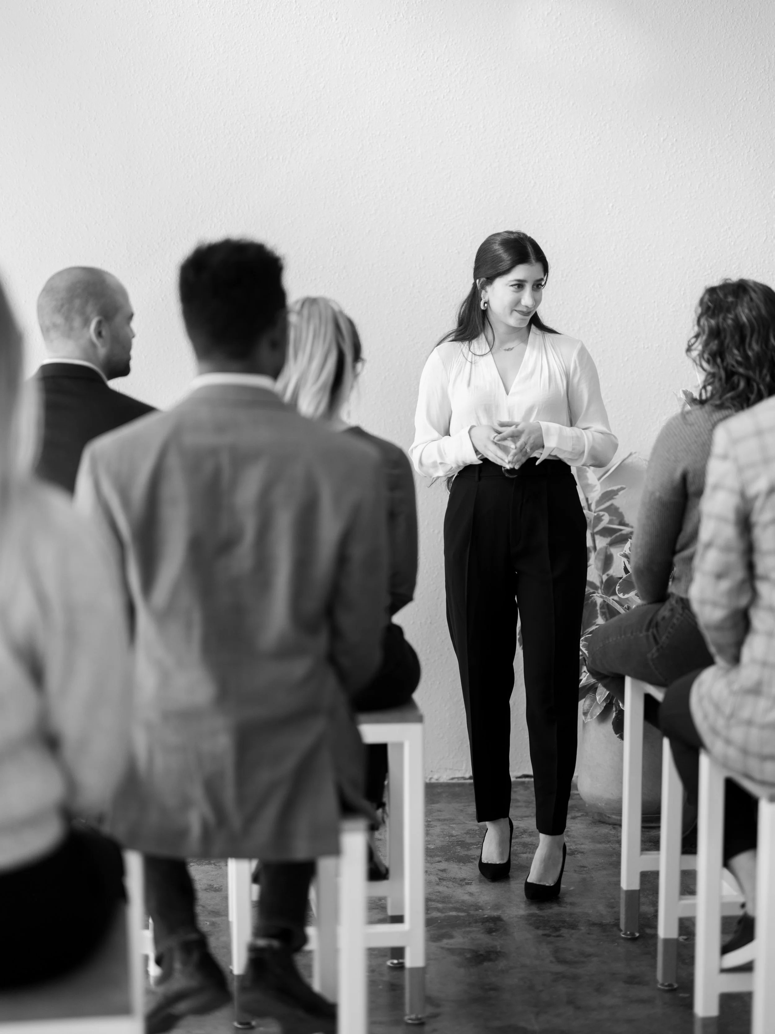 Woman speaking to an audience seated on stools in a casual setting, black and white photo.