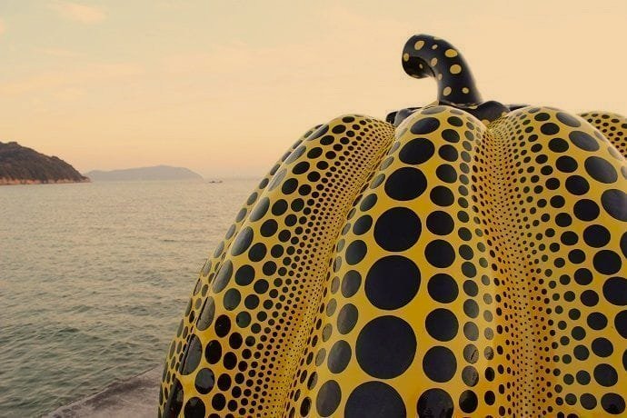 A large sculpture of a yellow and black spotted octopus on a beach with water and distant land in the background.