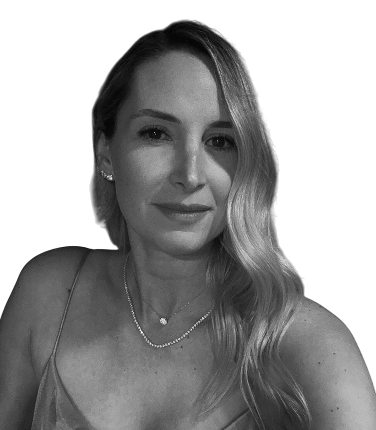 A woman with long wavy hair wearing a spaghetti strap top and layered necklaces, smiling at the camera with a plain background.