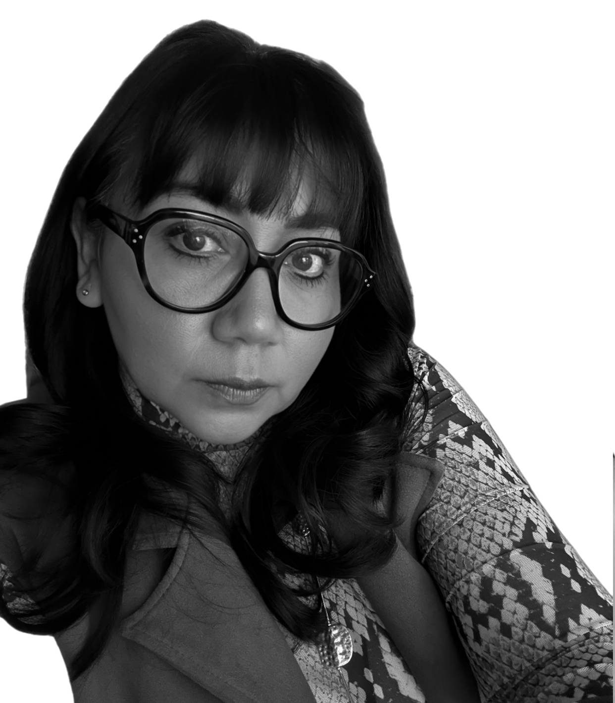 A woman with dark hair and glasses looking directly at the camera, wearing a patterned top and a jacket, against a plain background.