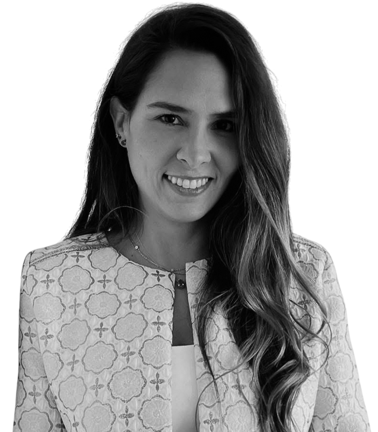 Black and white photo of a woman with long, wavy hair, smiling at the camera, wearing a patterned jacket over a top.