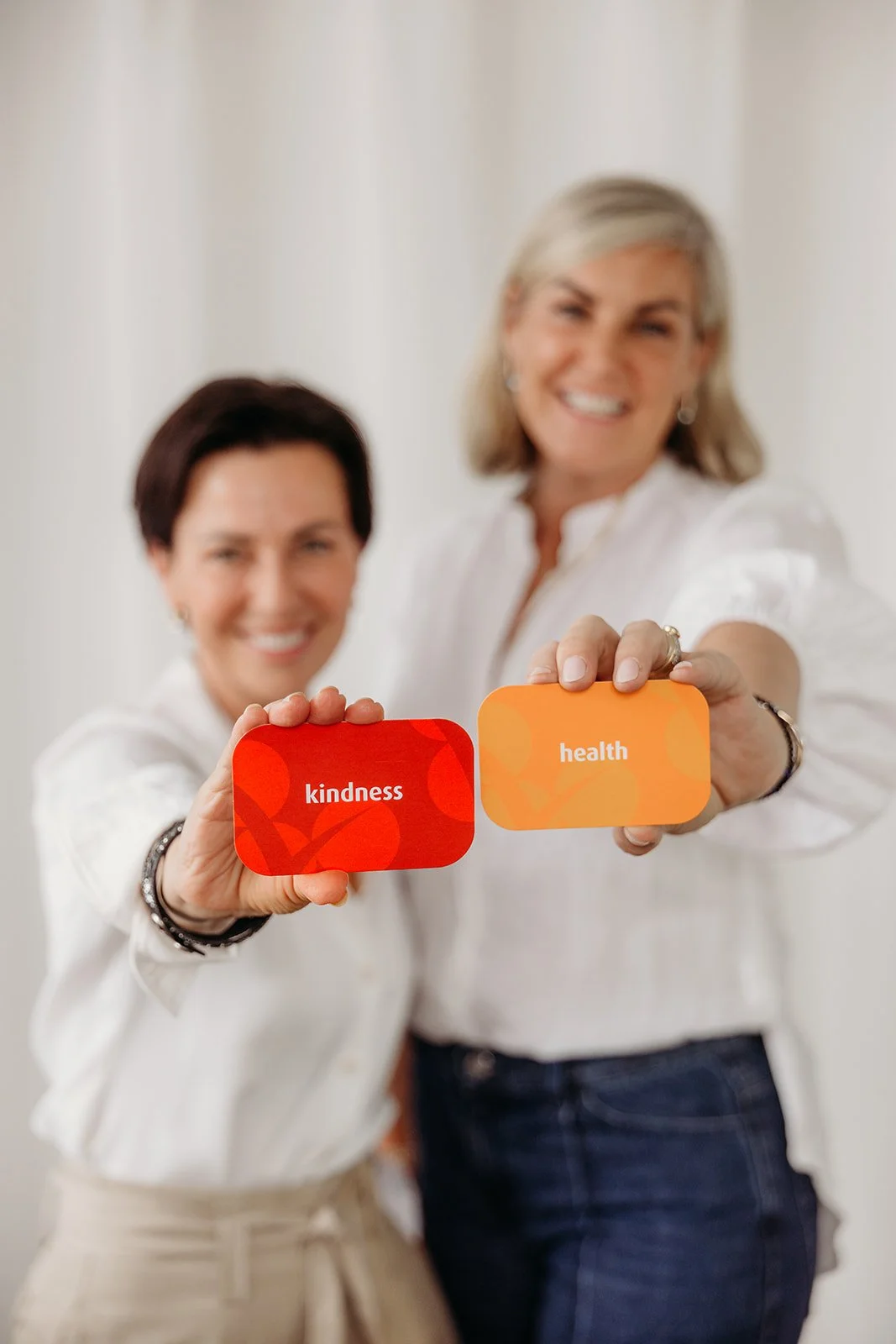 Two women smiling and holding cards that read 'kindness' and 'health' in front of them.