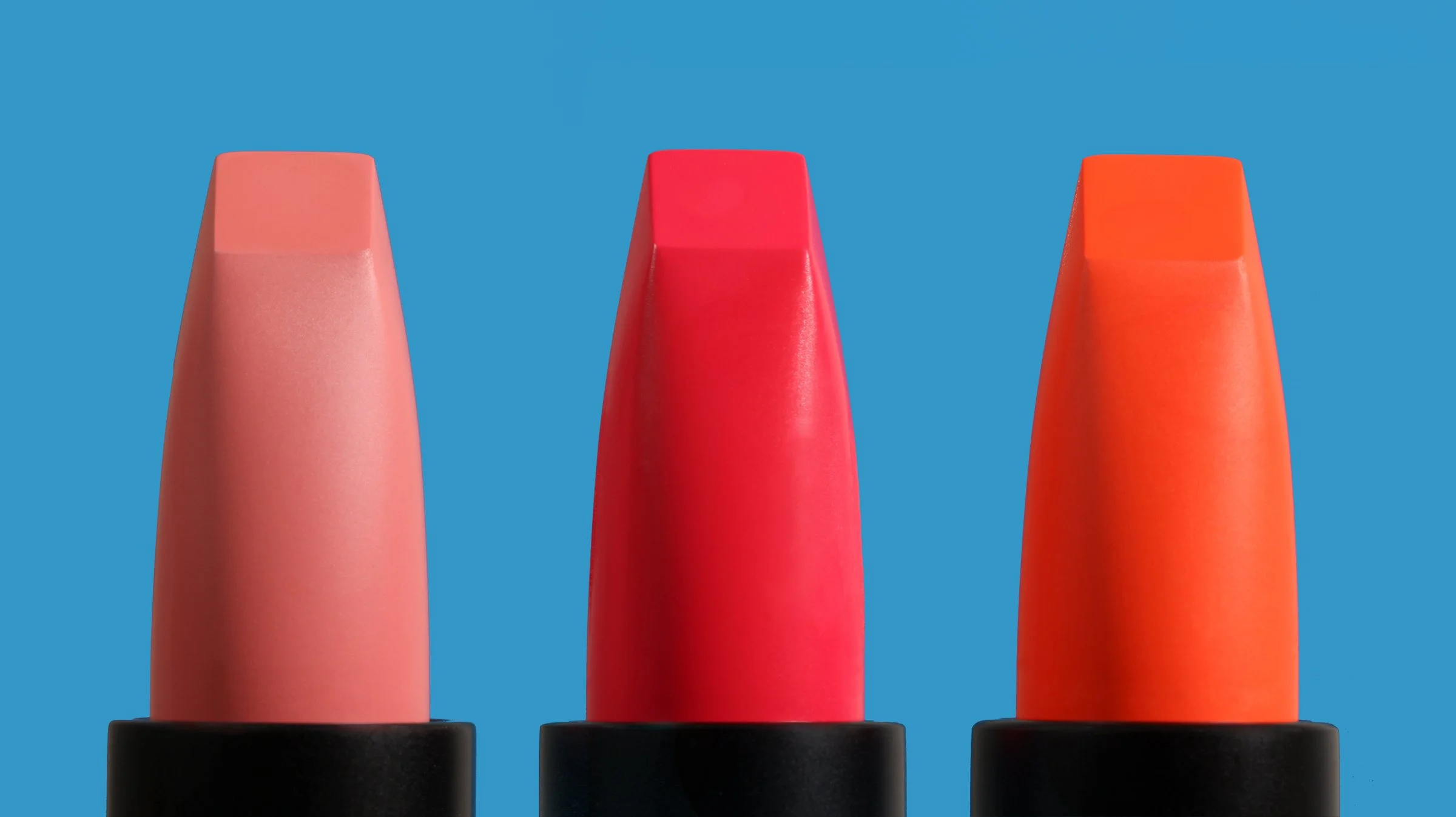 tre bullet rossetti colori accesi, rosa medio, fucsia e arancio acceso, forma squadrata moderna, su sfondo a contrasto turchese acceso, composizione minimalista naive che esalta i dettagli i colori e la forma geometrica dei rossetti, still life