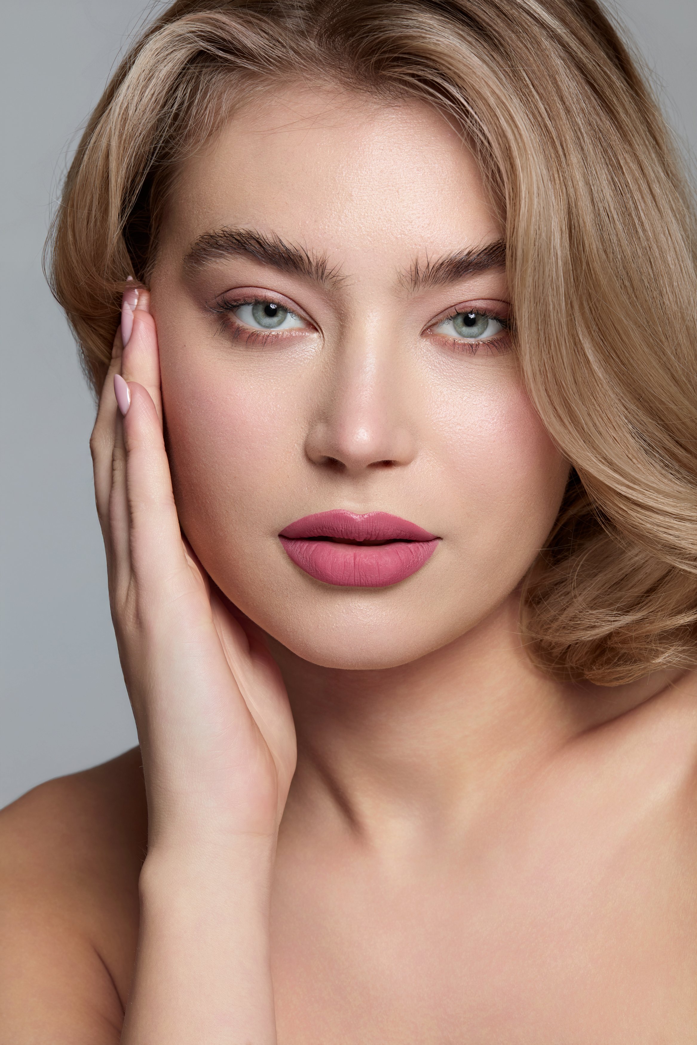 Modella bionda con occhi azzurri indossa un rossetto rosa intenso Splashtint Benefit Cosmetics, mani curate con smalto rosa, posa femminile, makeup femminile luminoso con focus su labbra definite e prodotto beauty in primo piano