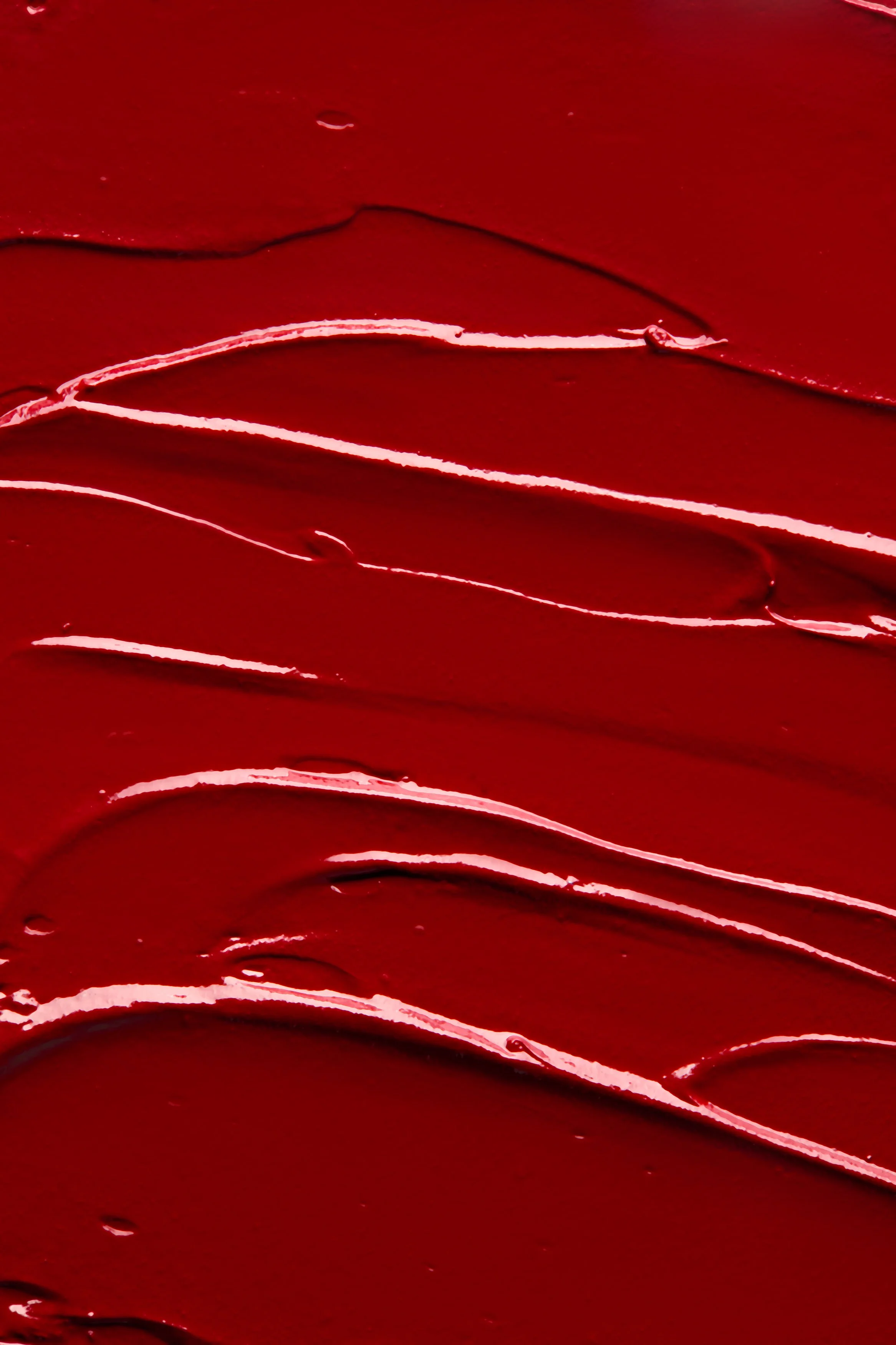 Spatolate di liquido rosso effetto rossetto liquido cremoso, ripresa dall’alto che valorizza texture densa, colore vibrante e movimento fluido in composizione artistica, fotografia textures cosmetiche