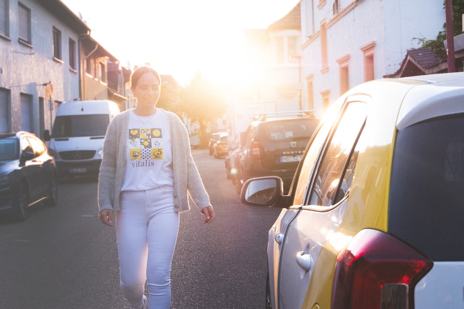 Eine junge Frau läuft an geparkten Autos auf einer Straße während des Sonnenuntergangs vorbei.