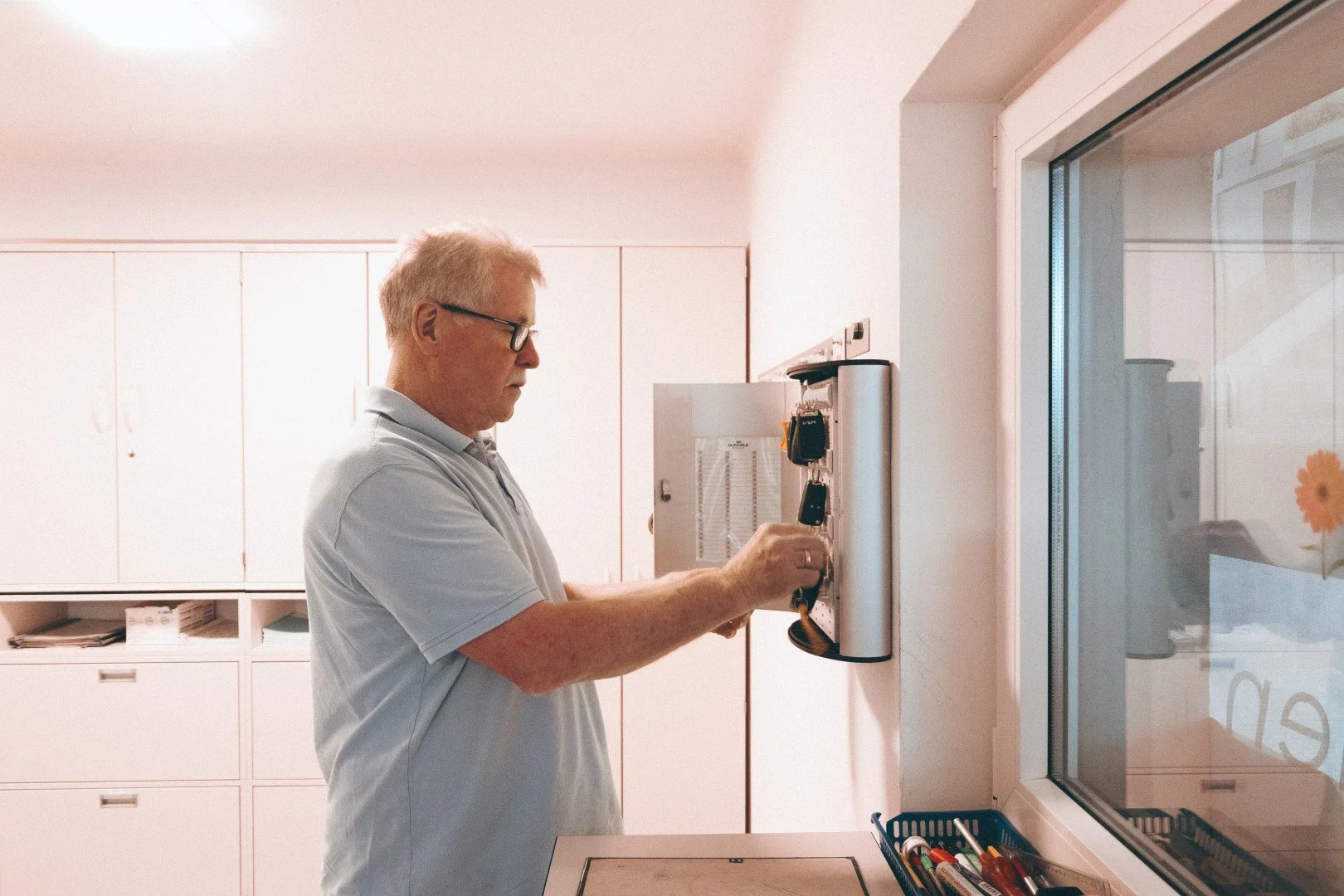Ein älterer Mann mit Brille arbeitet an einer Wand mit einem Klemmbrett und filmt.