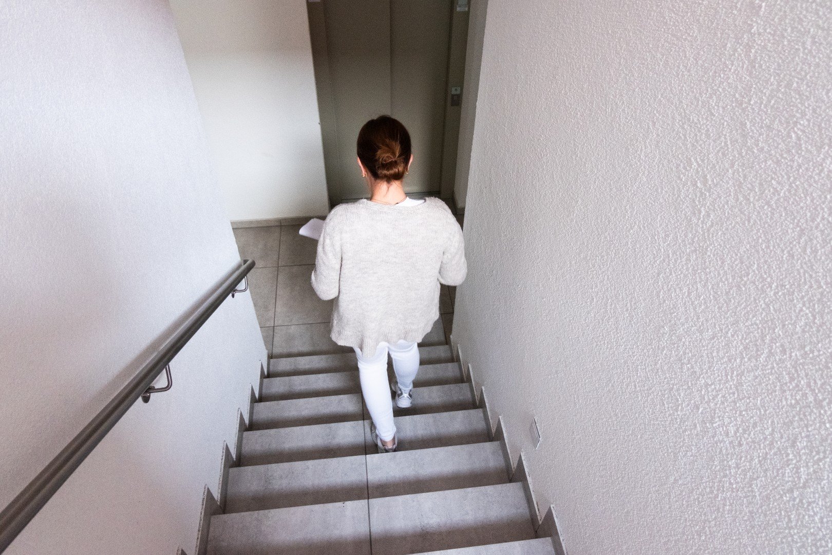 Eine Frau in weißem Pullover und weißen Hosen geht die Treppe im Haus hinunter.