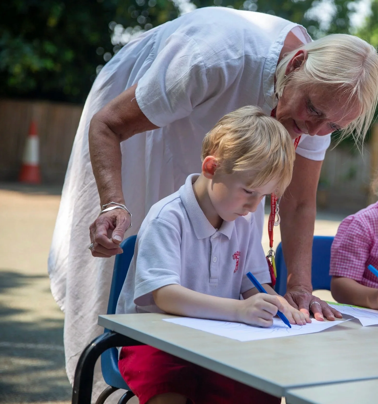 A teacher assisting young children with a drawing activity outdoors at a school event.