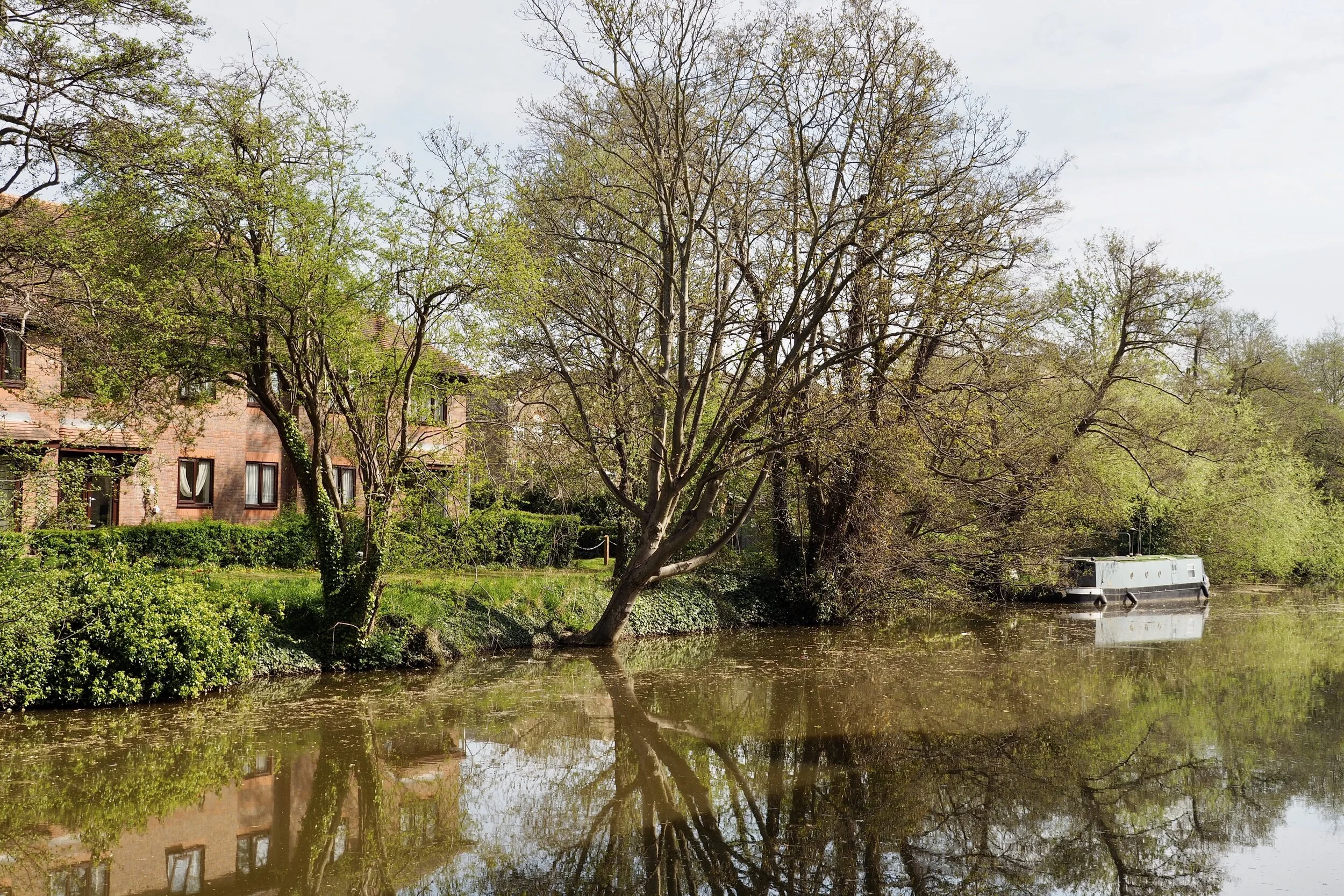Riverside scene with a brick house, trees, and a boat.