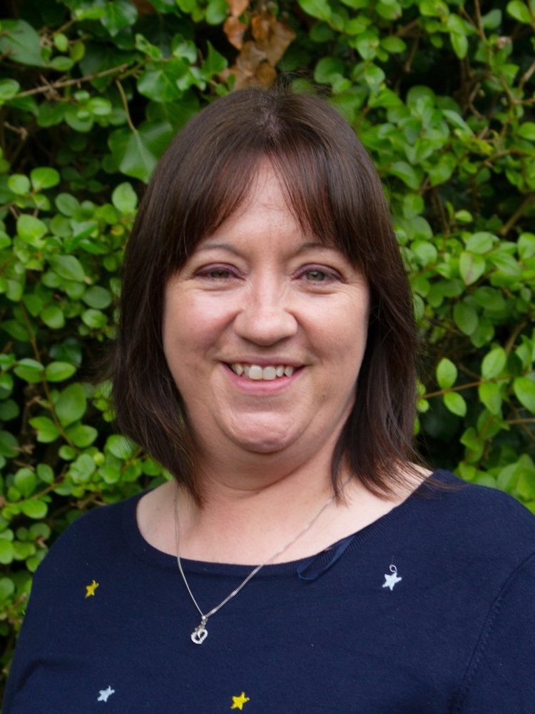 Woman smiling in front of a leafy green background