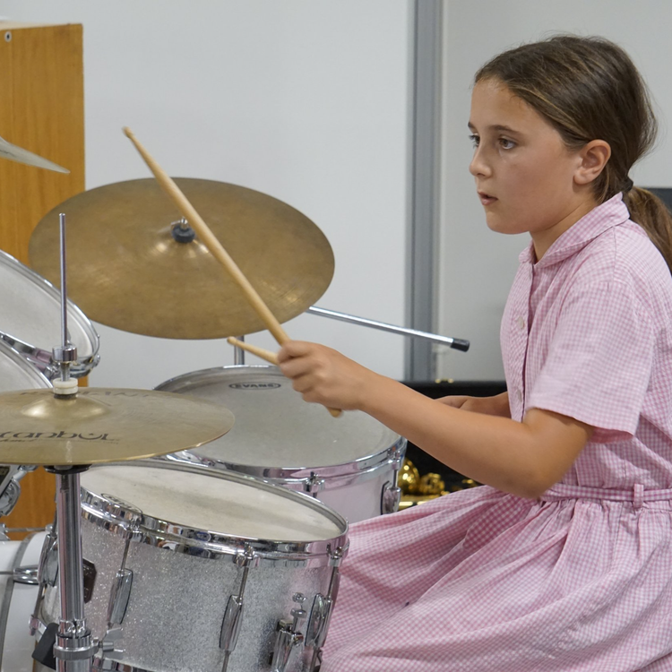 A young girl playing the drums in a pink dress.