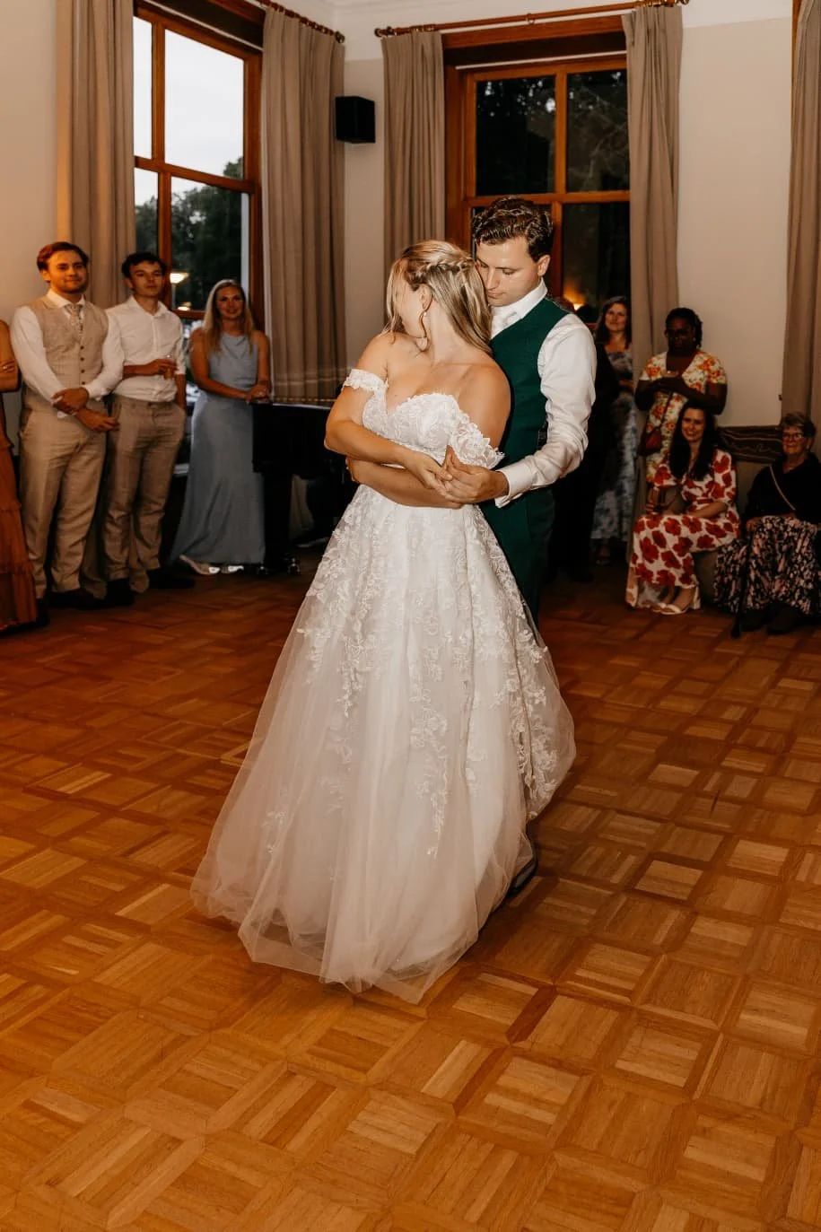 A bride and groom dancing at their wedding reception with friends and family watching indoors.