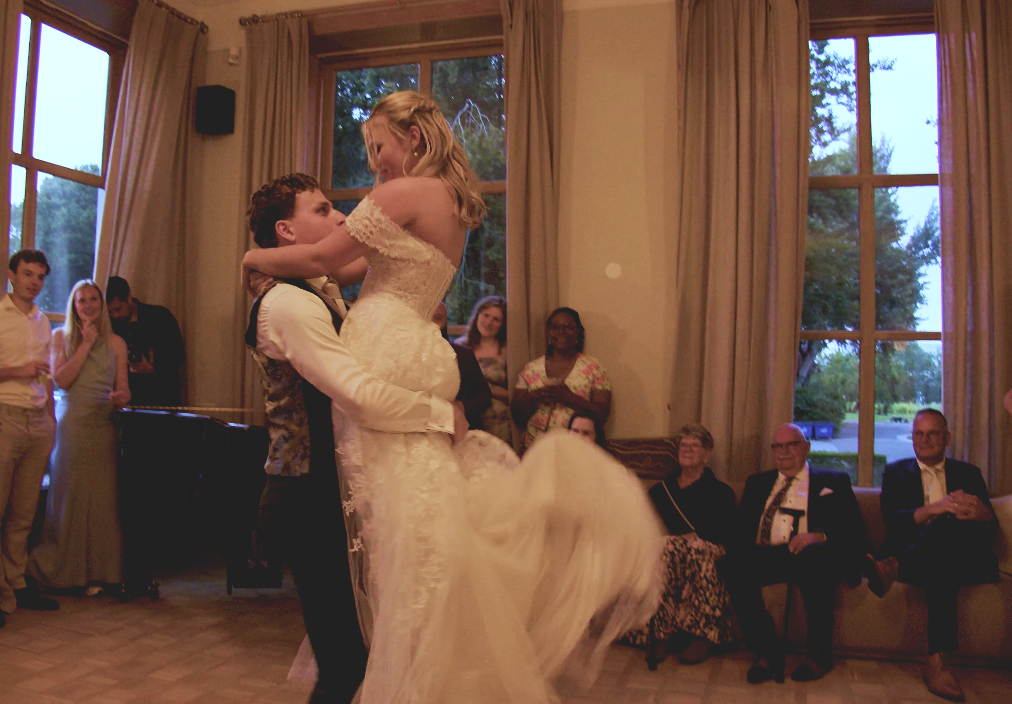 A bride and groom dancing at their wedding reception with friends and family watching indoors.