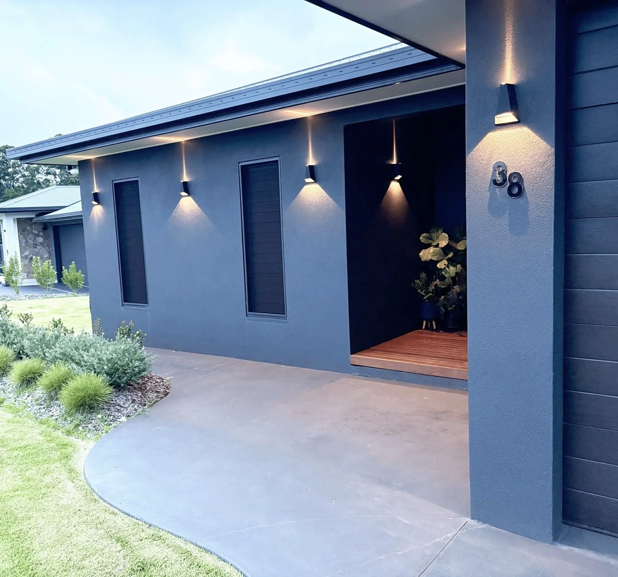 Modern house with dark blue exterior walls, black windows, outdoor lighting, and a small porch area with plants