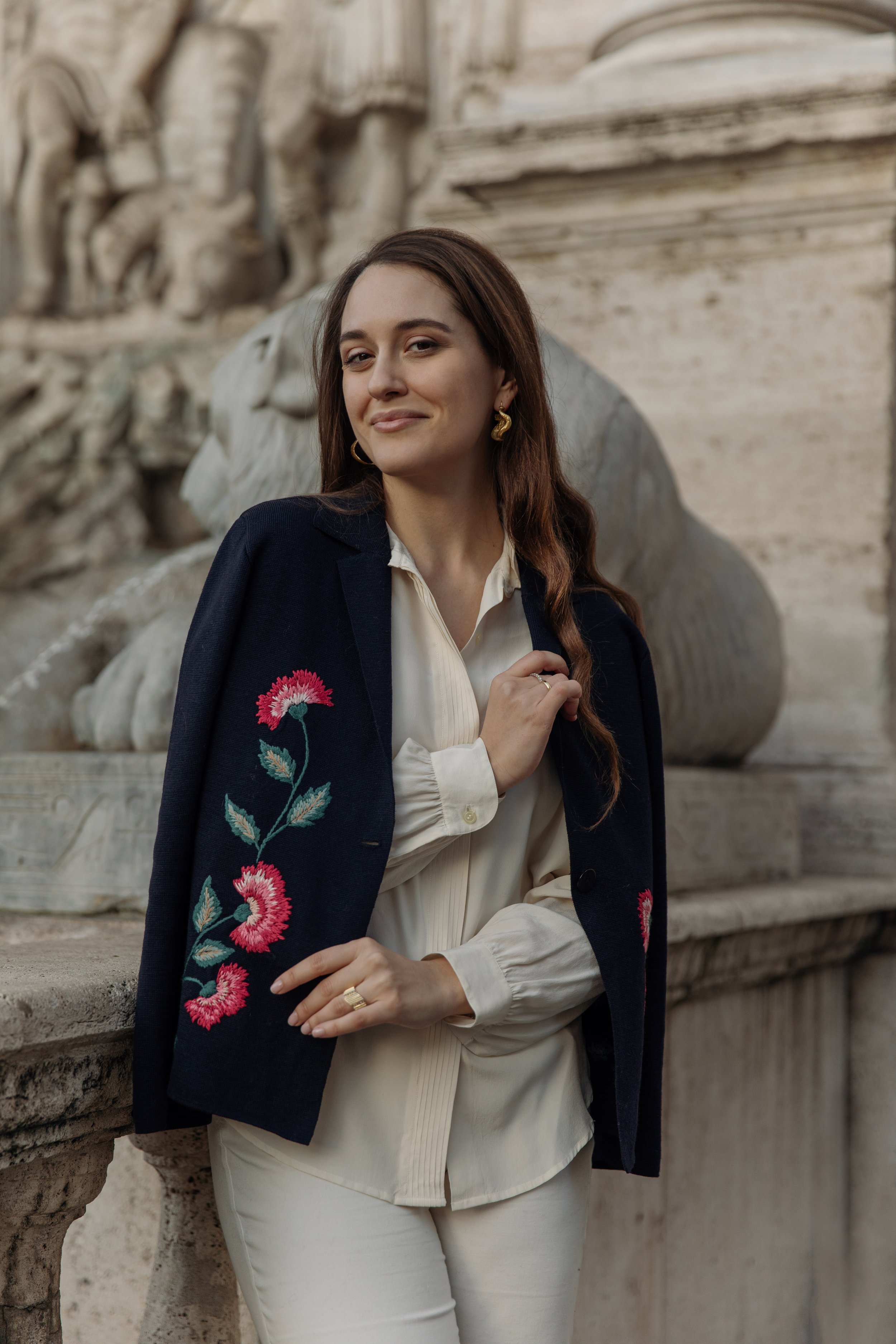 Donna sorridente con una giacca elegante, sfondo con scultura in pietra.