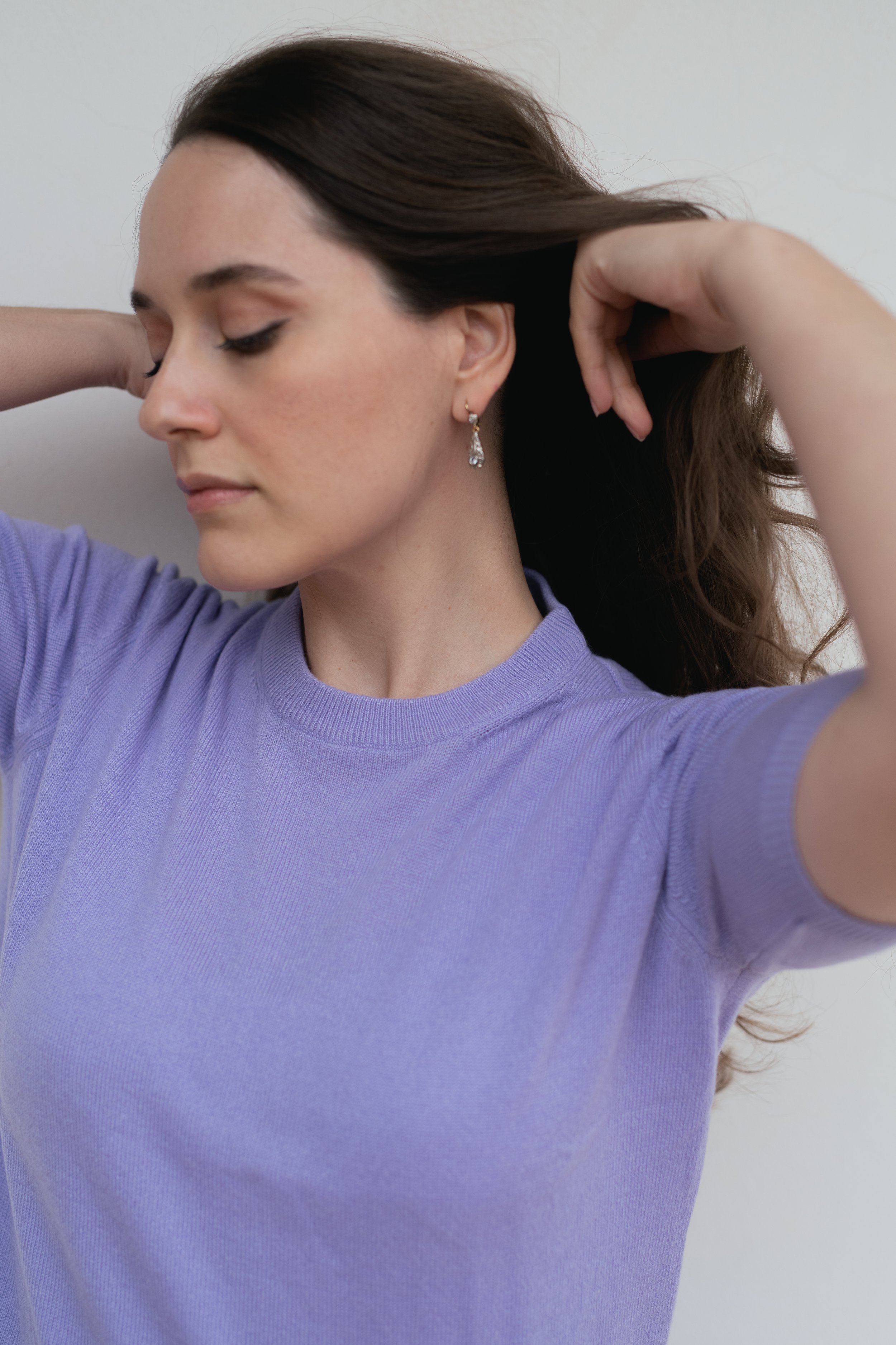 Donna con maglione viola toccandosi i capelli.