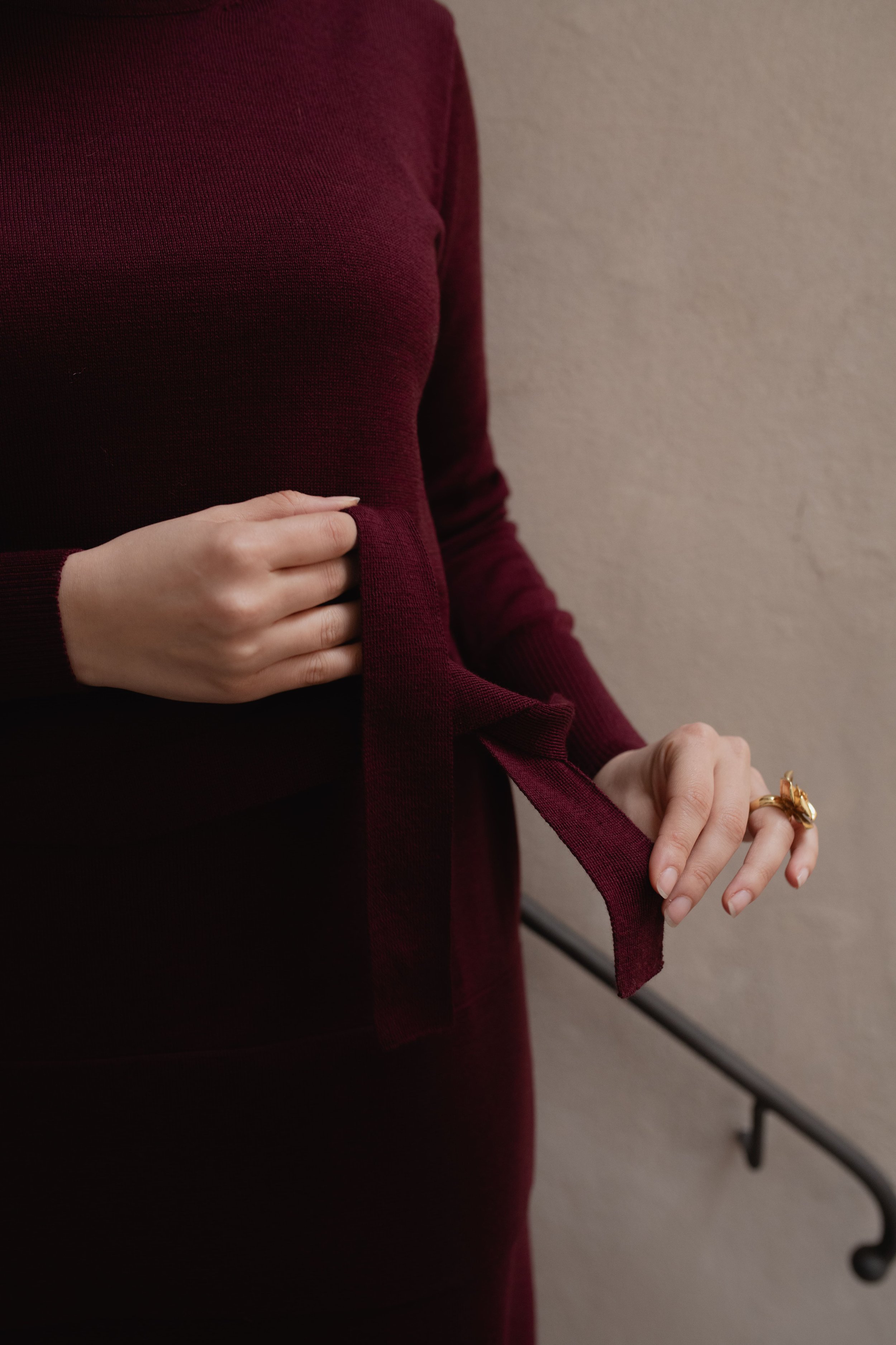 Persona con maglione bordeaux che annoda una cintura, anello dorato su una mano.