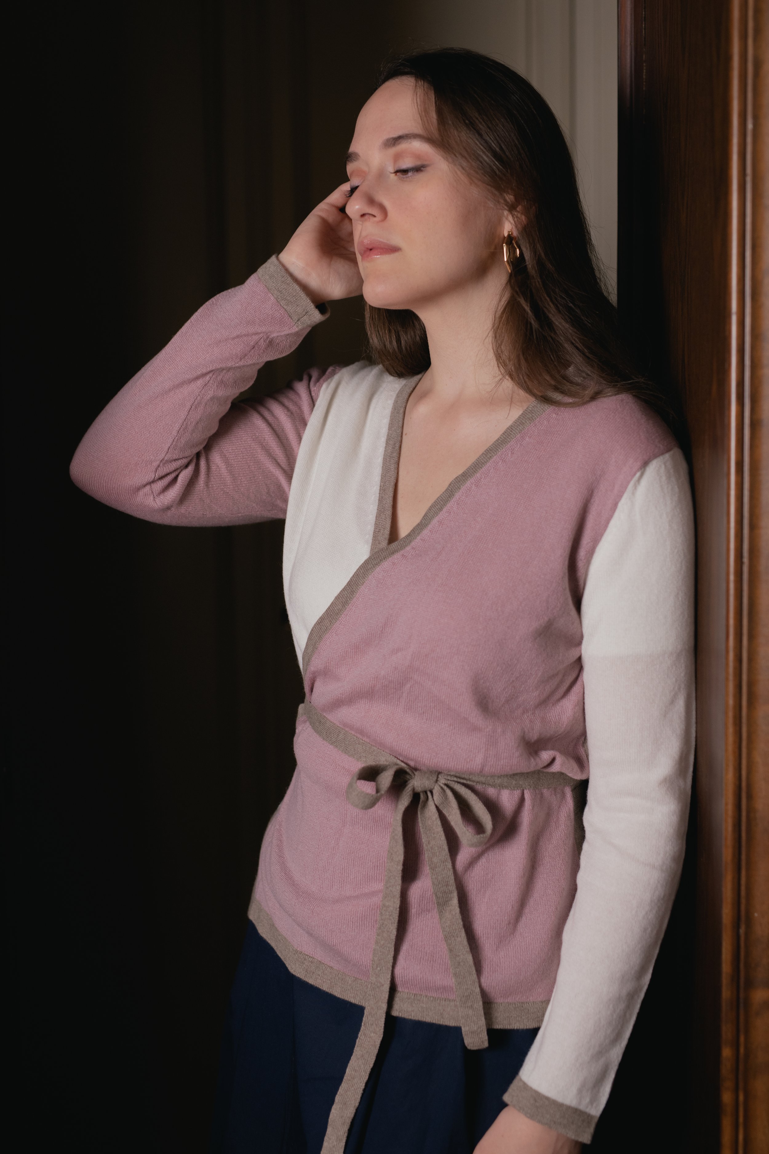 Donna con maglione rosa e bianco, occhi chiusi, appoggiata a un muro