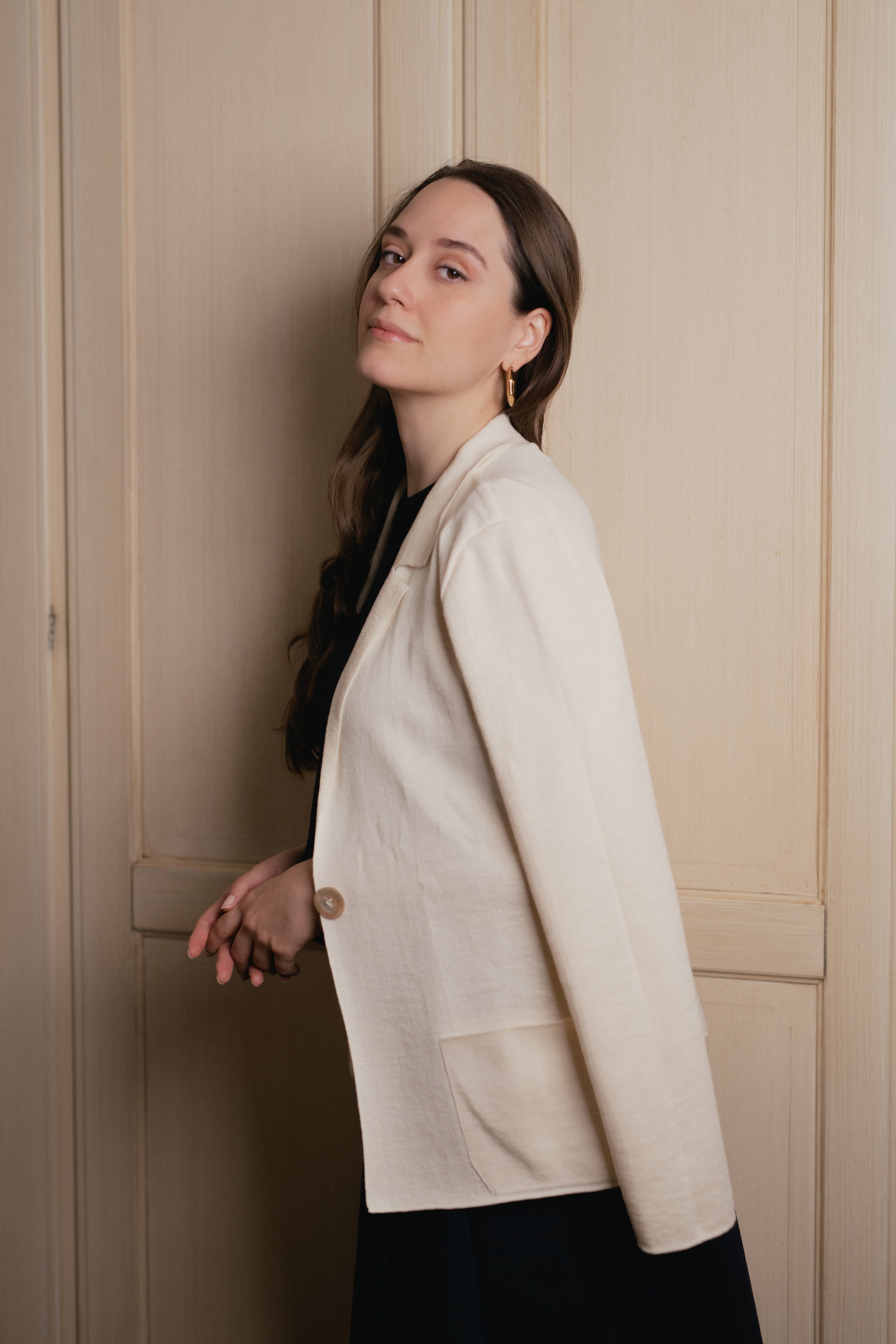 Donna con blazer beige in posa davanti a una porta di legno.