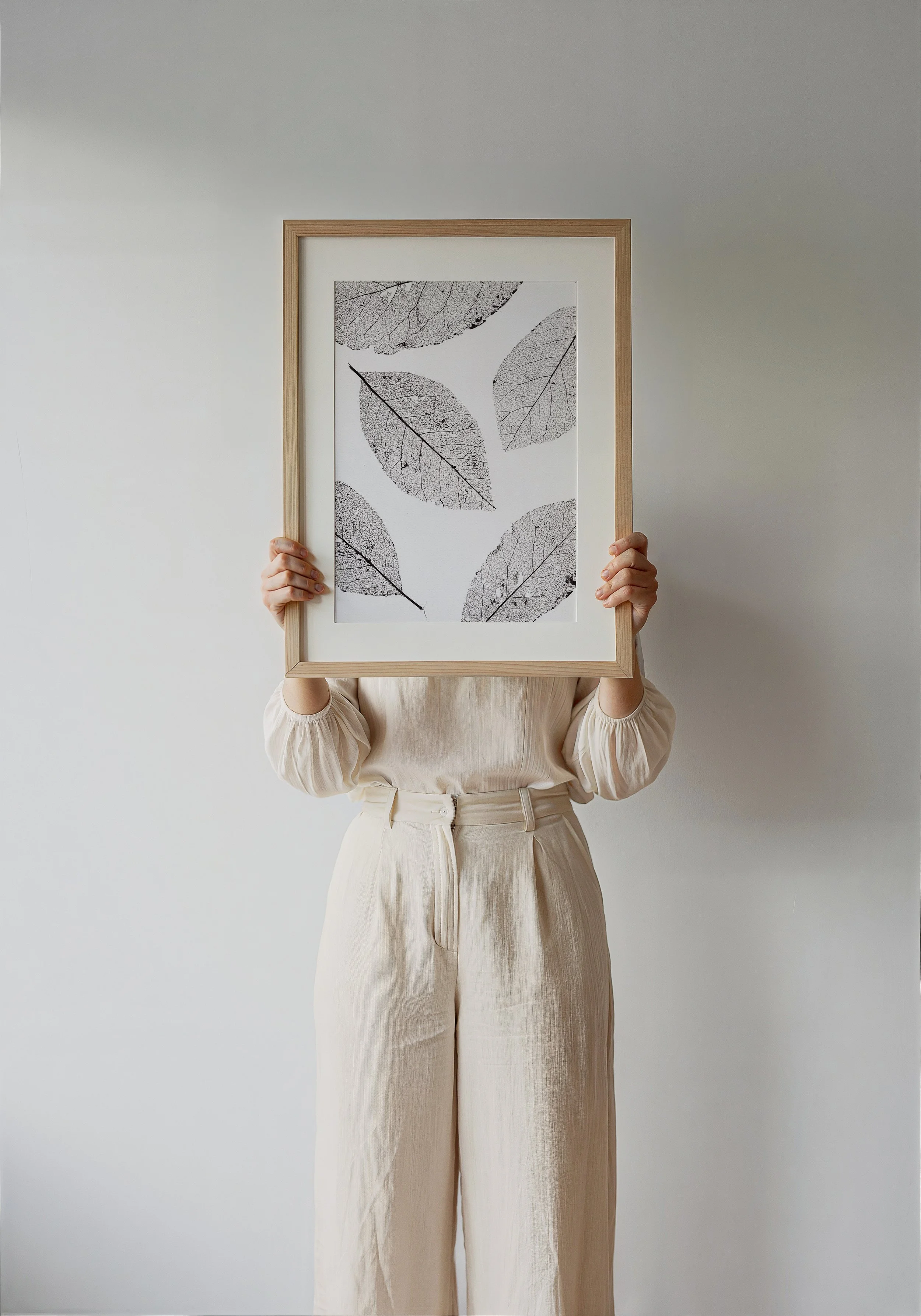 Person holding a framed artwork of black and white leaves against a plain white background.