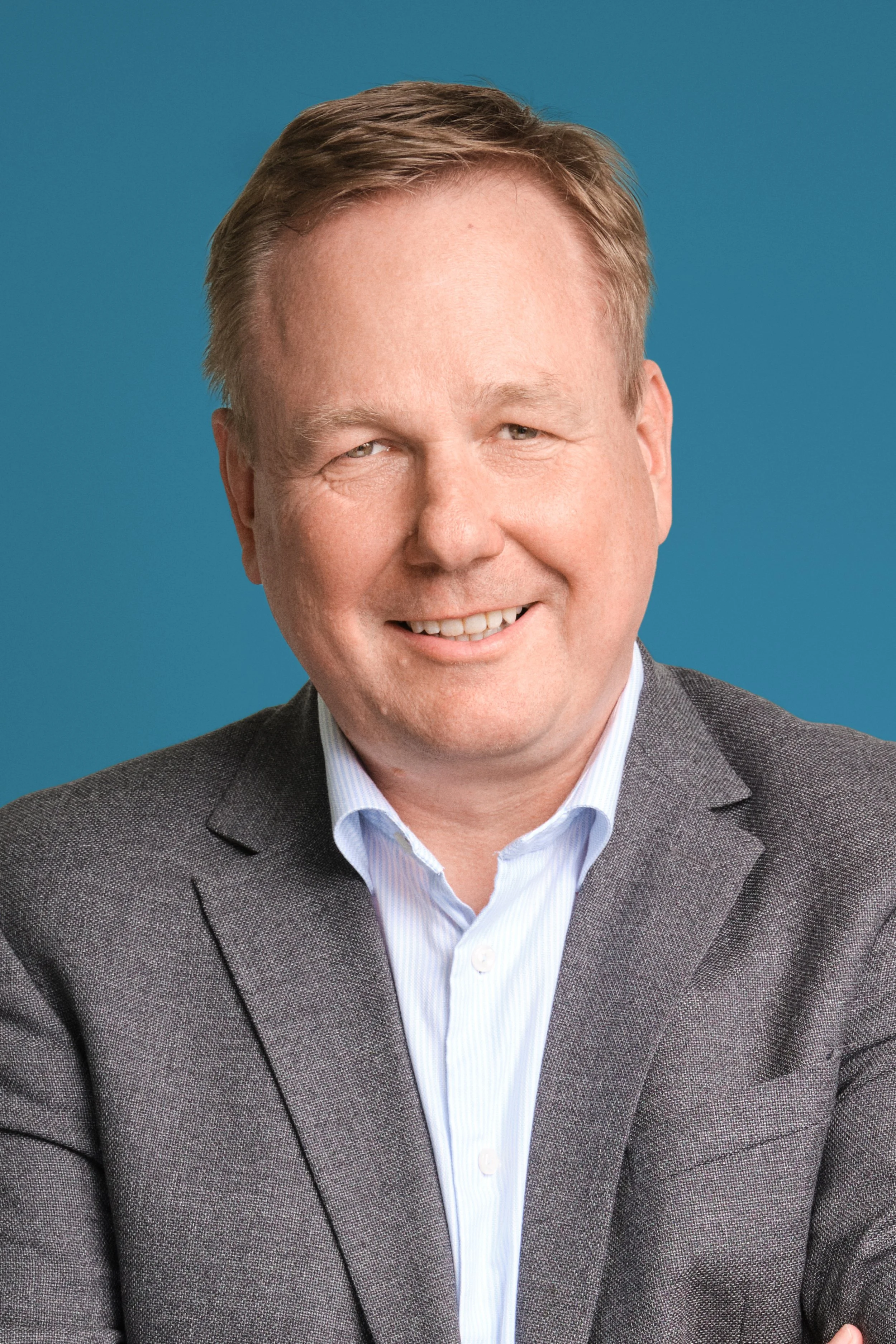 Portrait of a smiling man in a gray suit and white shirt against a blue background.