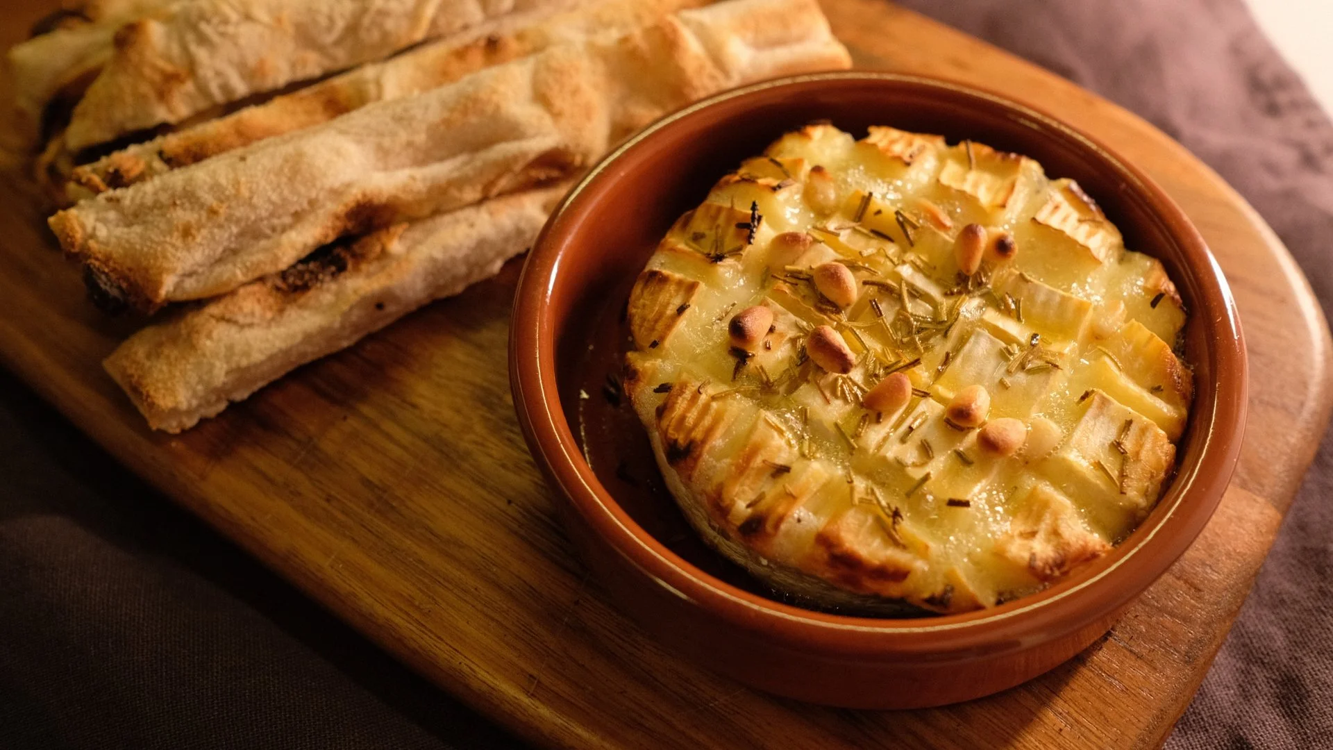 En smilende kvinne med brunt hår i en bar eller restaurant med flasker på hyller bak henne.